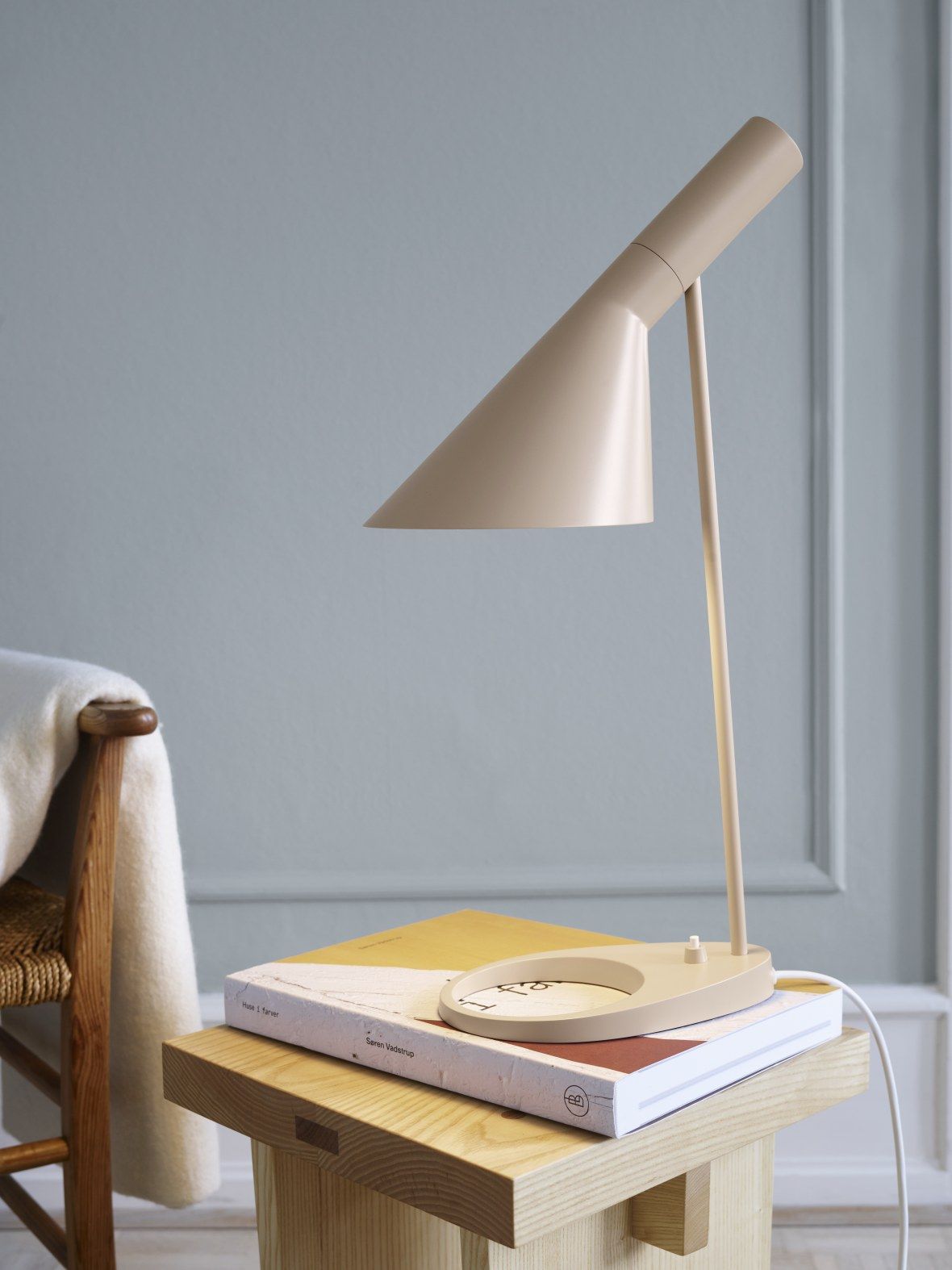Beige AJ Tischleuchte von Louis Poulsen auf einem Nachttisch mit Büchern, modernes Design.