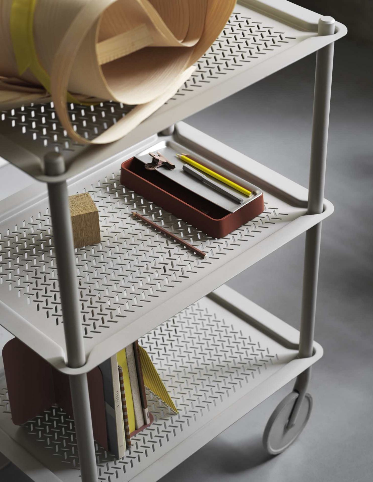 Detailaufnahme des grauen Flow Trolley Servierwagens von Muuto mit drei Ablageflächen und diversen Büroartikeln.