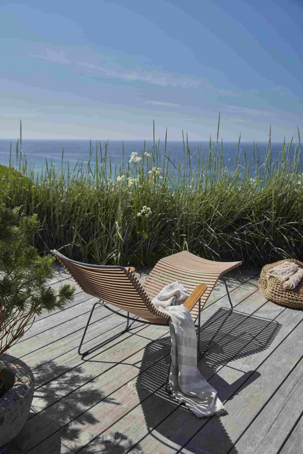 Click Sunrocker Sonnenliege von Houe: Dunkelgraue Outdoor Liege mit Decke auf Holzterrasse am Meer.