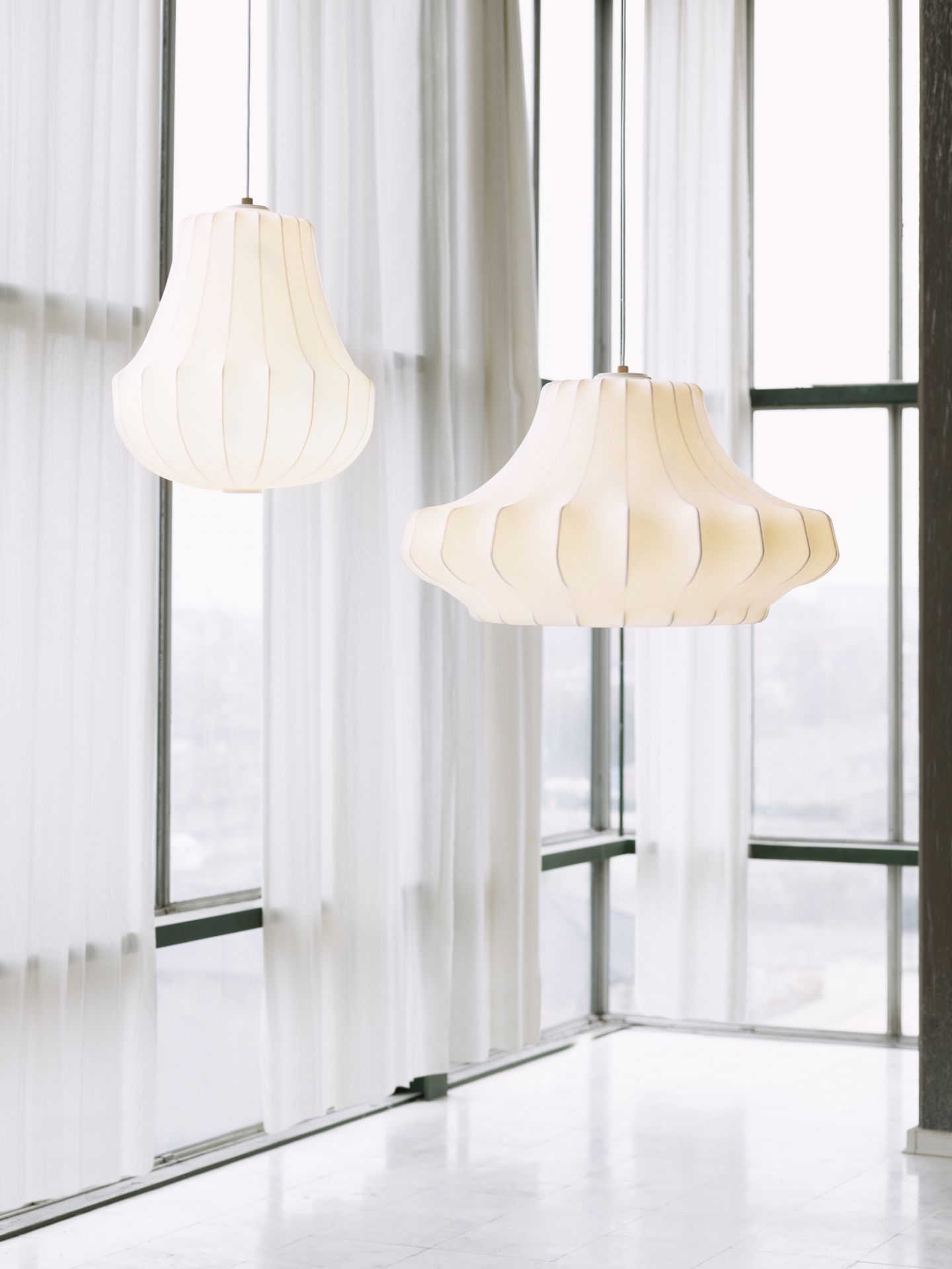 Zwei große, weiße Phantom Pendelleuchten von Normann Copenhagen hängen vor einem Fenster.