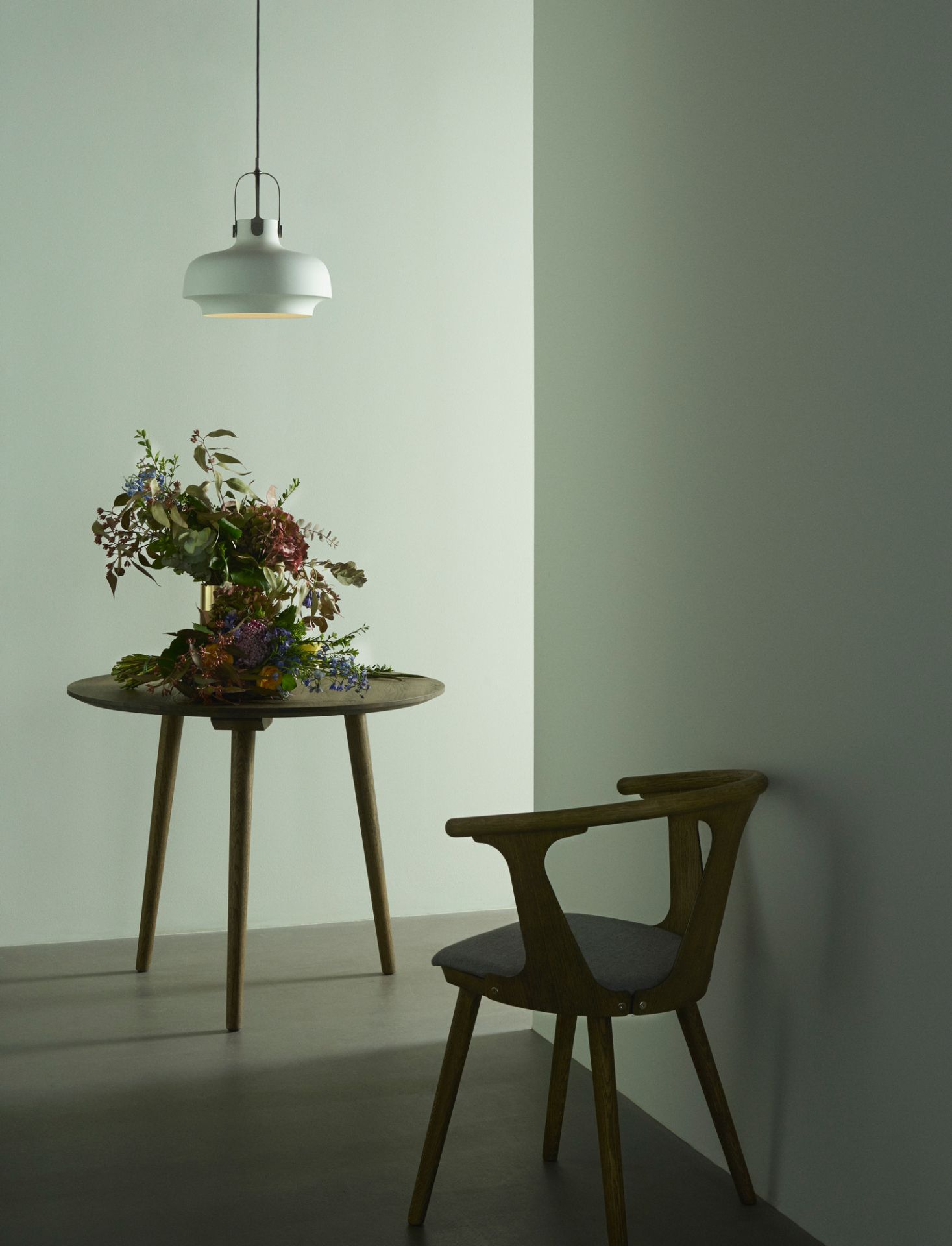 AndTradition In Between Chair SK1, schwarz lackierter Holzstuhl mit grauem Sitzpolster in minimalistischem Raum.