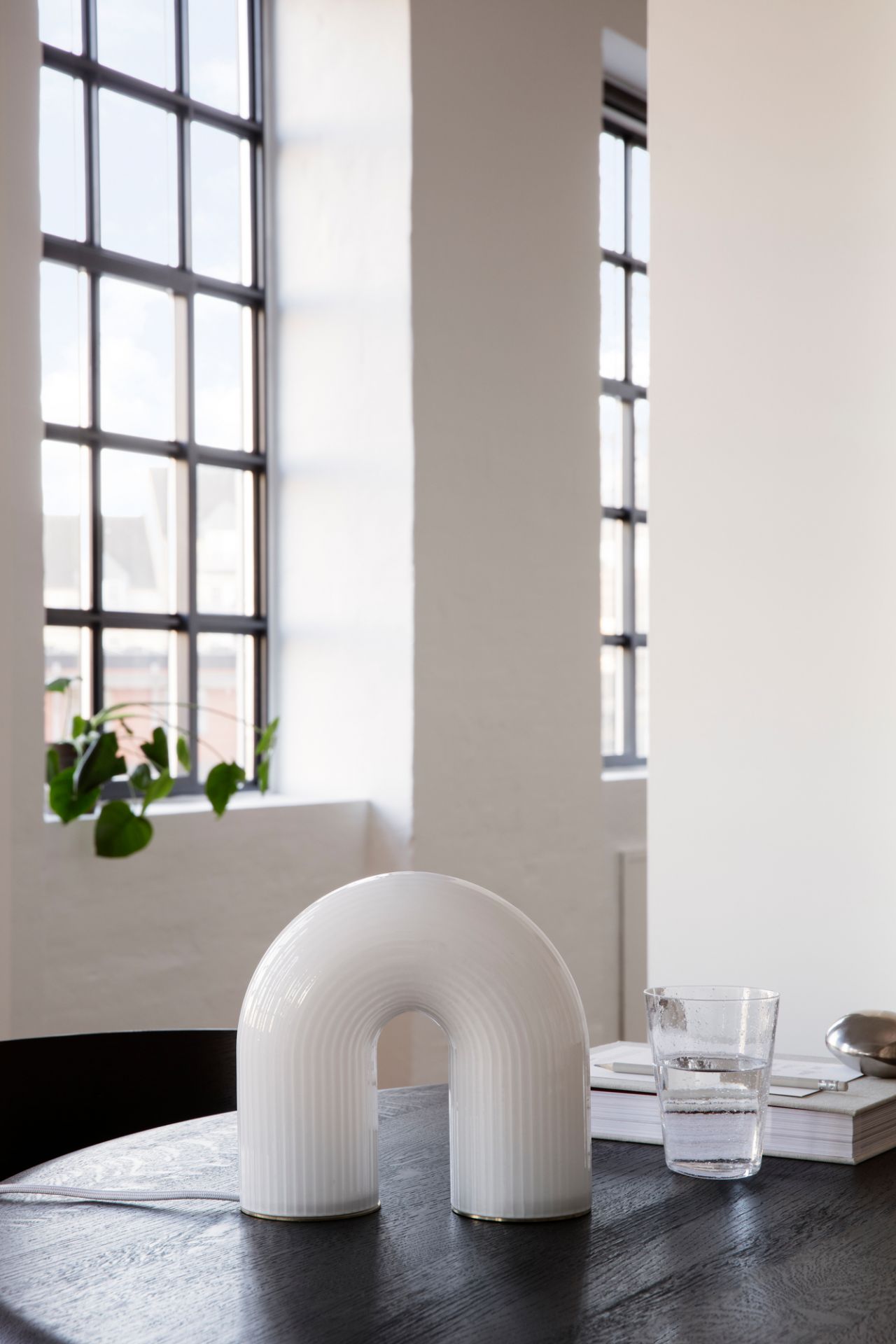 Nahaufnahme der Ferm Living Vuelta Tischleuchte, eine moderne Bogenlampe aus Opalglas auf dunklem Holztisch.