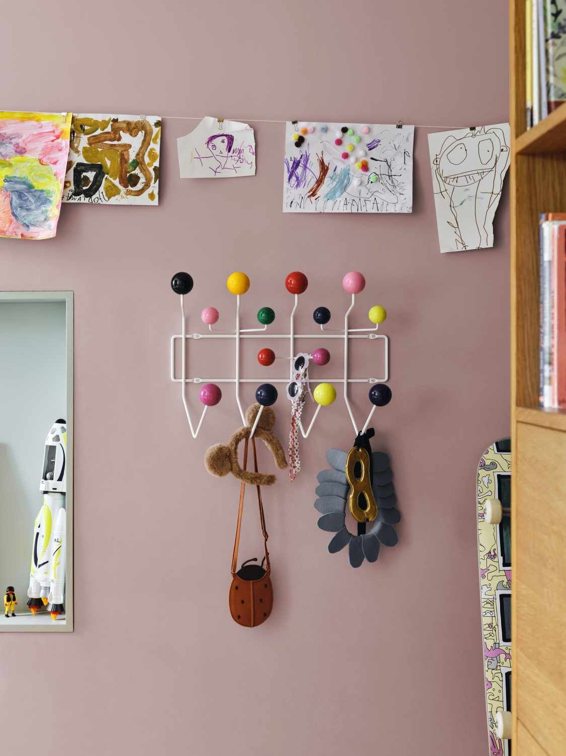 Eames Hang it all Garderobe von Vitra mit bunten Kugeln und Kinderzeichnungen an rosa Wand.
