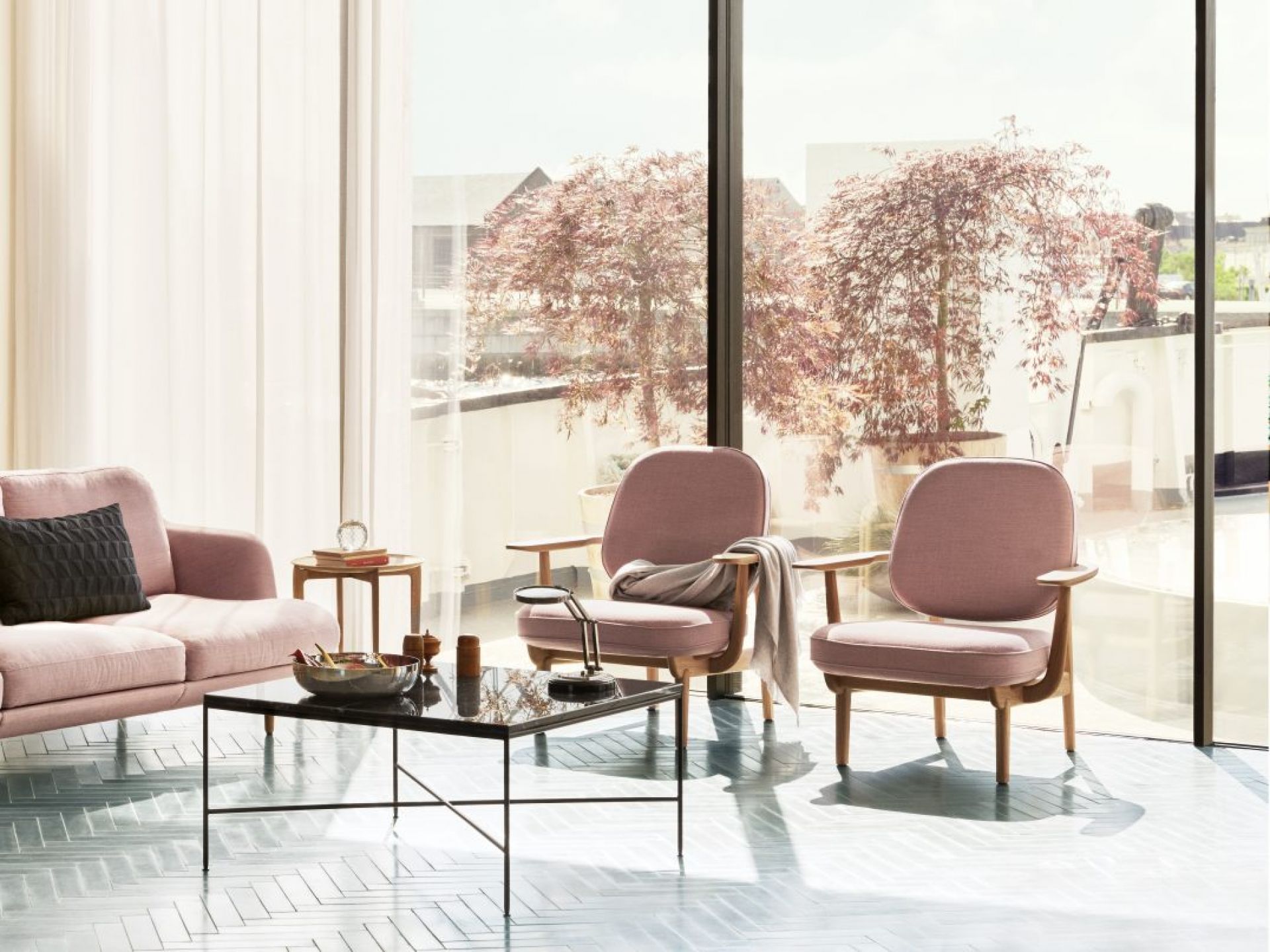 Heller Wohnraum mit Fritz Hansen Fred Loungesessel in Rosa, Sofa, Tisch und großem Fenster mit Baum.