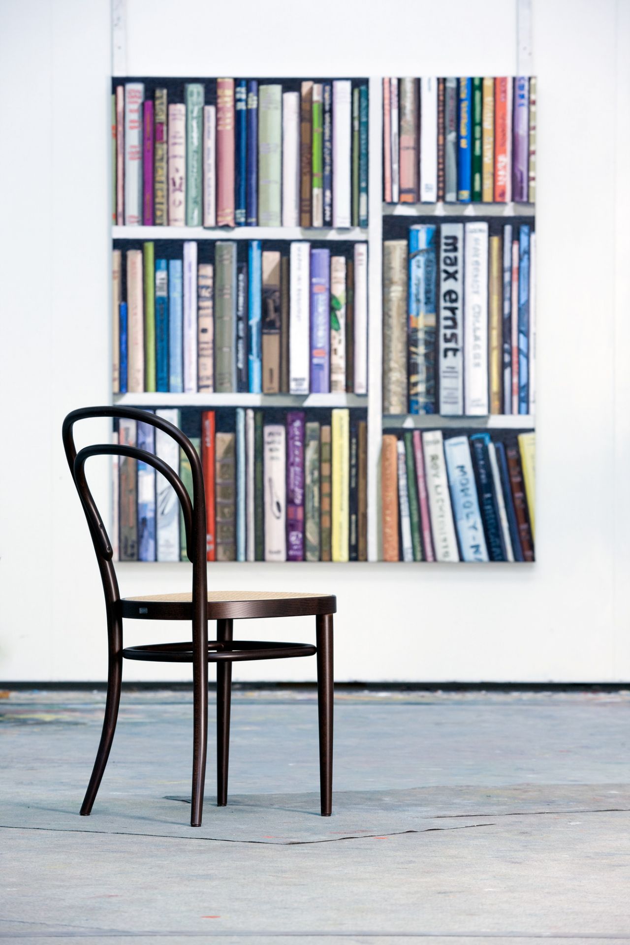 Brauner 214 Bugholzstuhl, ein Thonet Kaffeehausstuhl mit Wiener Geflecht, vor einem Bücherregal-Gemälde.