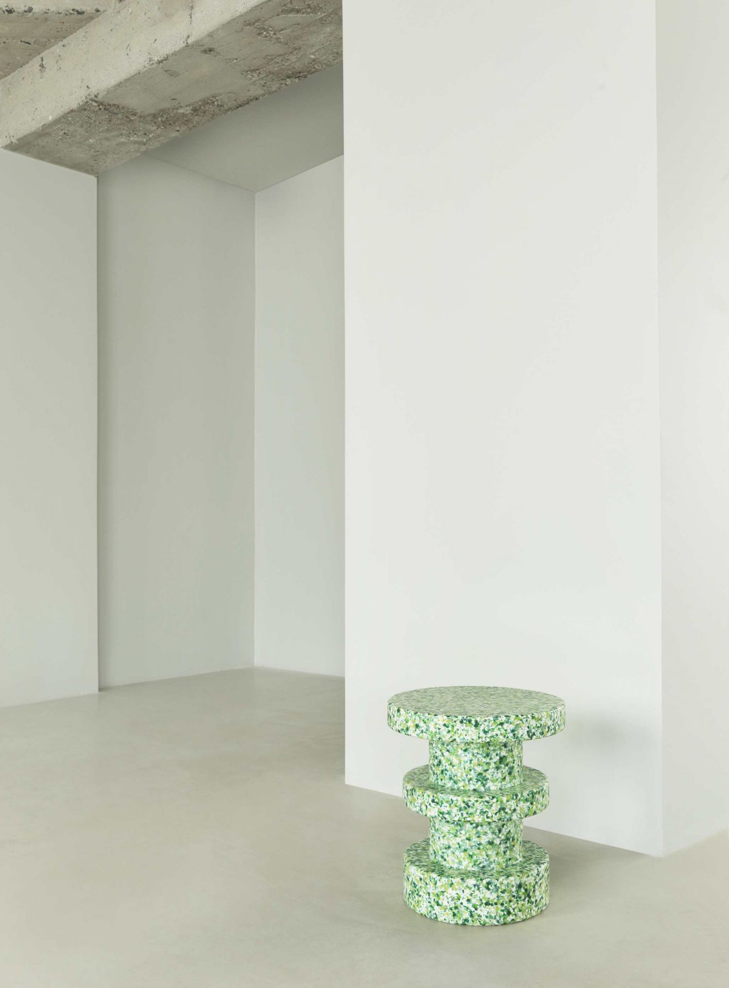 Normann Copenhagen Bit Stool Stack Hocker in Grün-Weiß gesprenkelt vor weißer Wand und Betonboden.