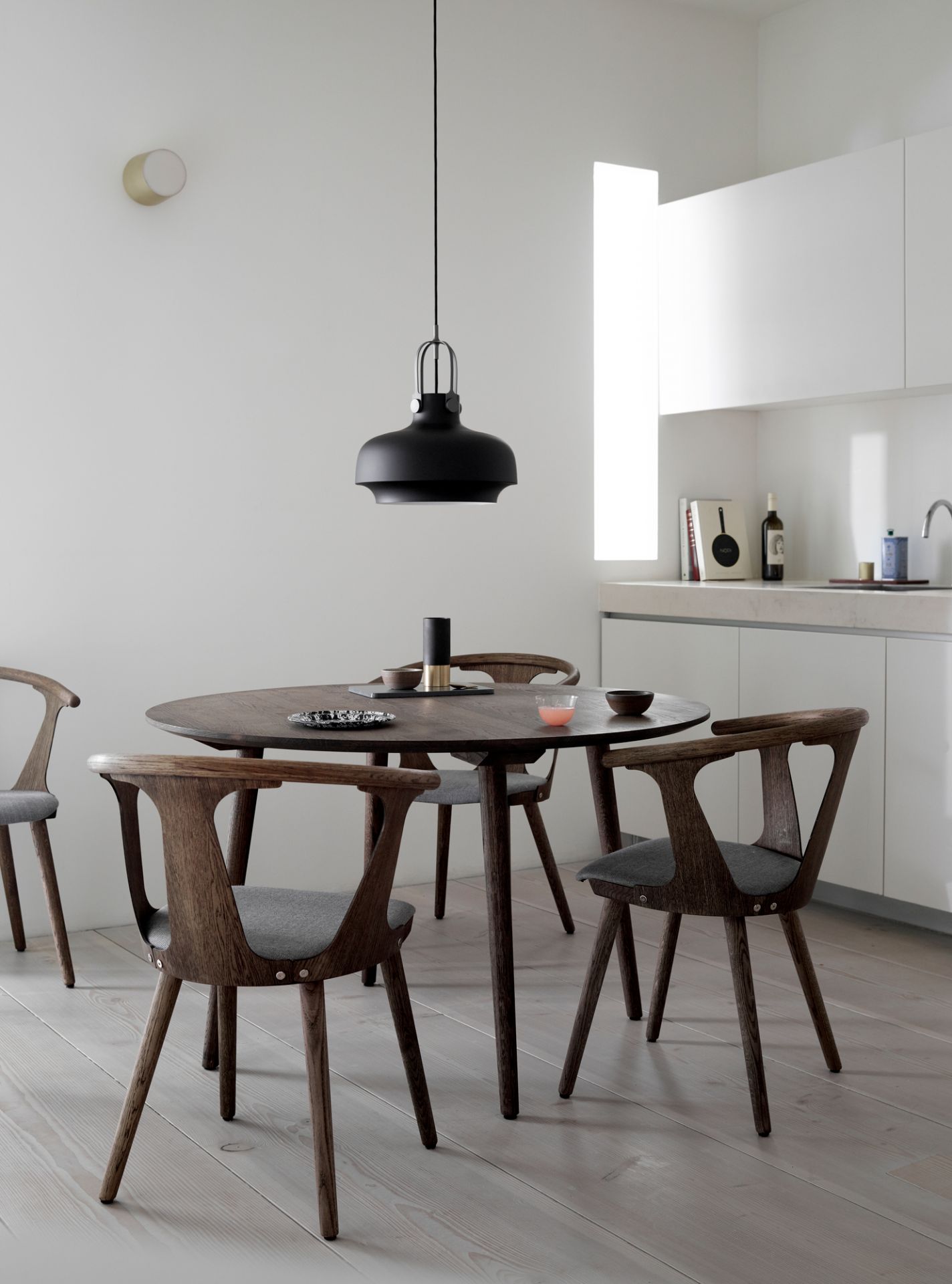 Schwarze Copenhagen SC7 Pendelleuchte von AndTradition über einem Esstisch mit Holzstühlen in einem hellen Raum.
