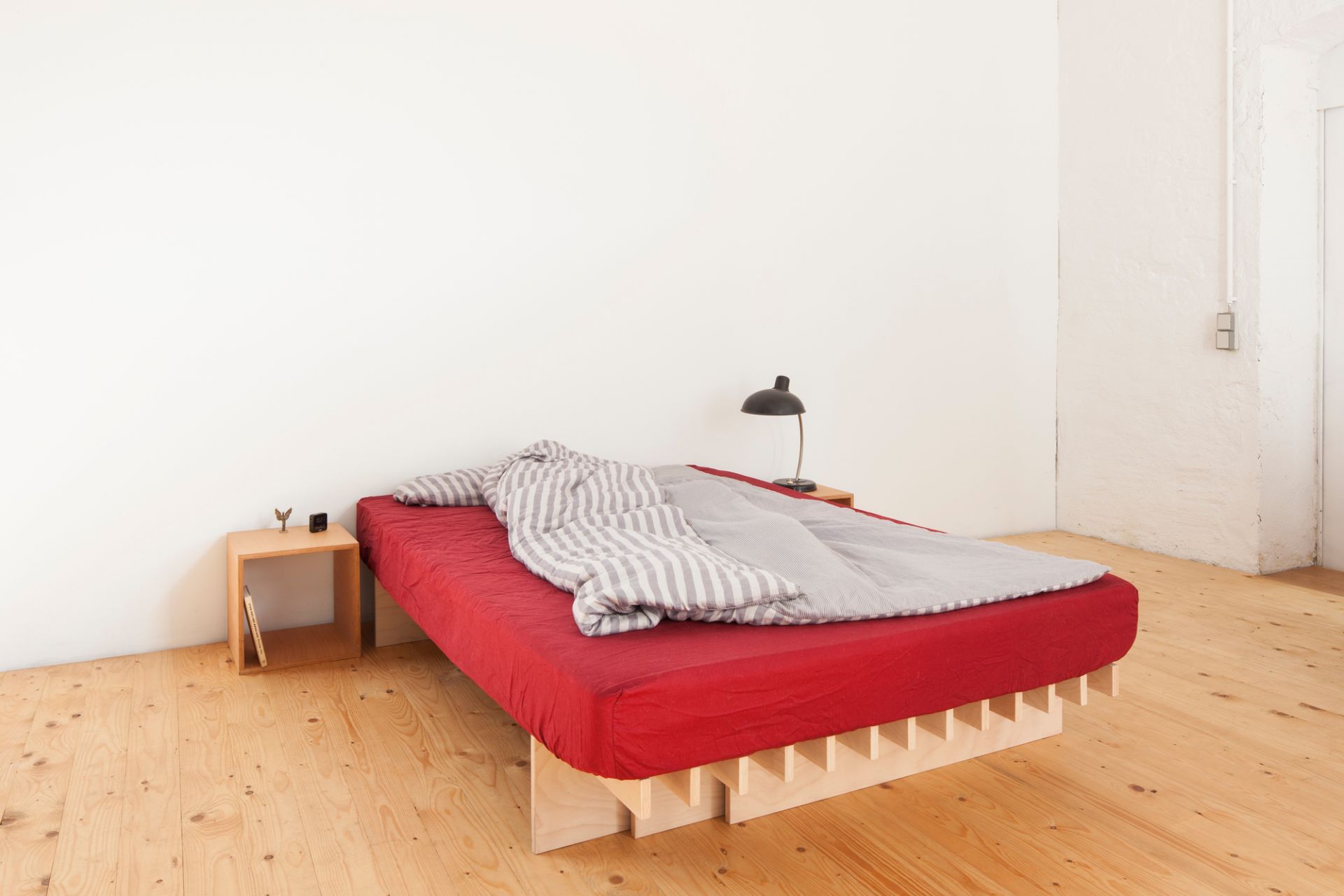 Cube Nachttisch von Tojo neben einem Bett mit roter Bettwäsche und einer Lampe.