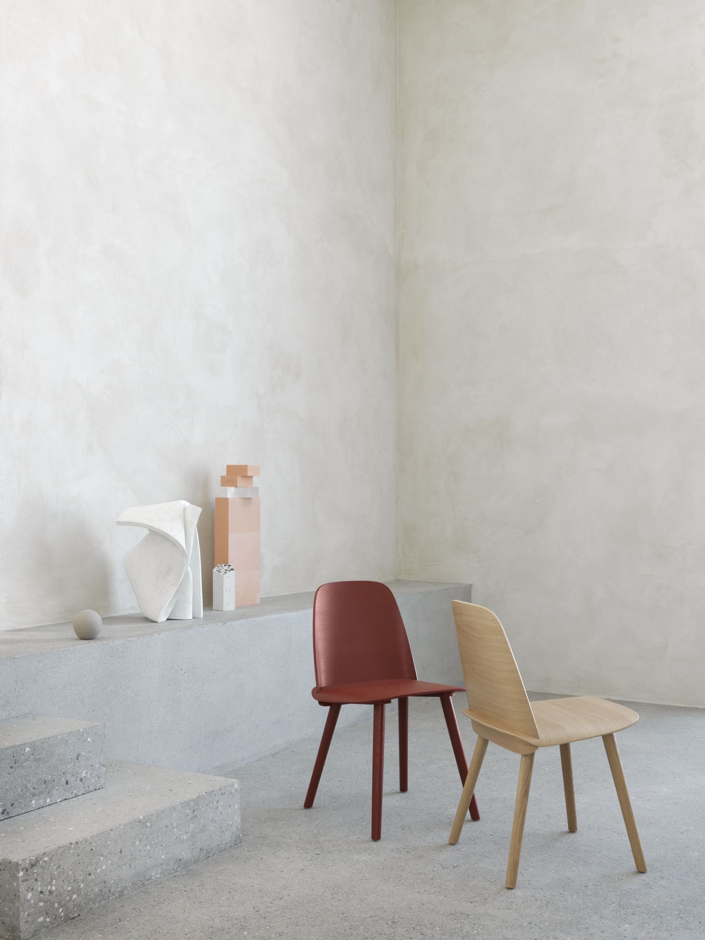 Zwei Muuto Nerd Chairs: ein Holzstuhl und ein rotbrauner Stuhl im minimalistischen Interieur.