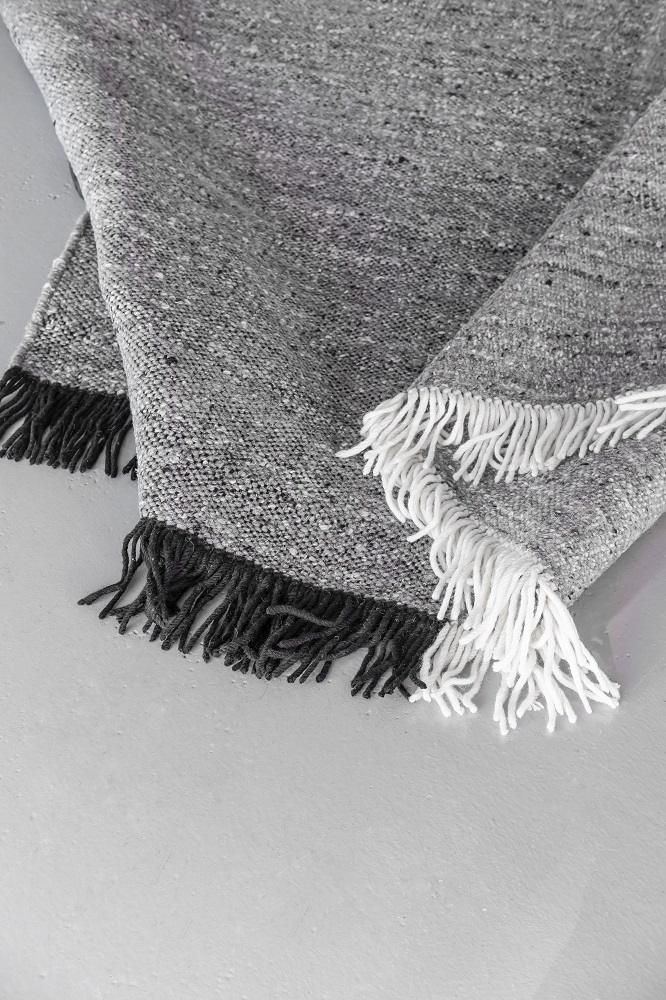 Detailaufnahme des Nanimarquina Re-Rug Teppichs in Grau mit schwarzen und weißen Fransen.