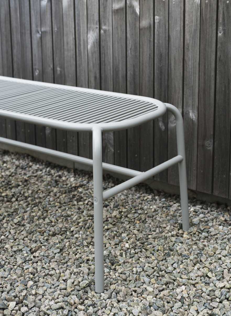 Graue Vig Bank von Normann Copenhagen für den Außenbereich vor Holzwand und Kies.