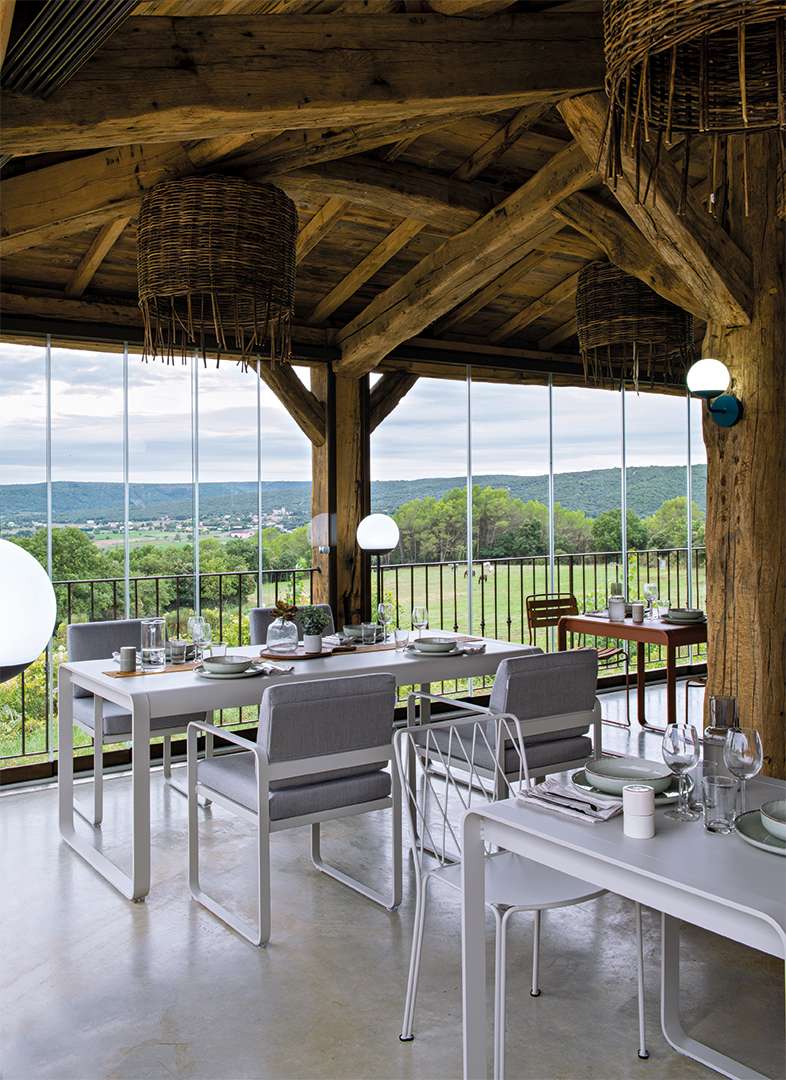 Bellevie Sessel von Fermob auf einer Terrasse mit Esstisch und malerischer Aussicht ins Grüne.