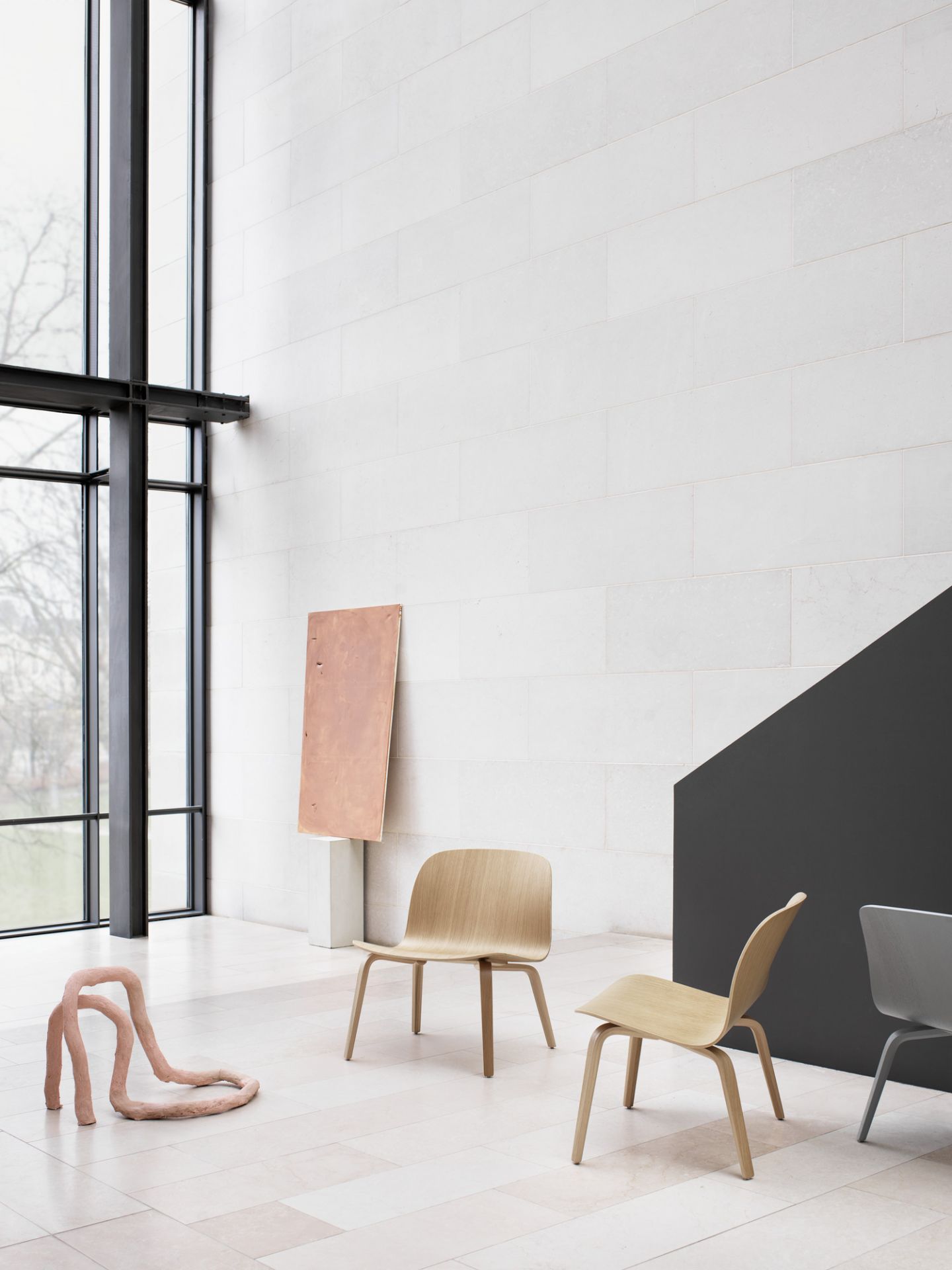 Muuto Visu Lounge Chair Stuhl aus Holz in heller Umgebung mit Kunstobjekten.