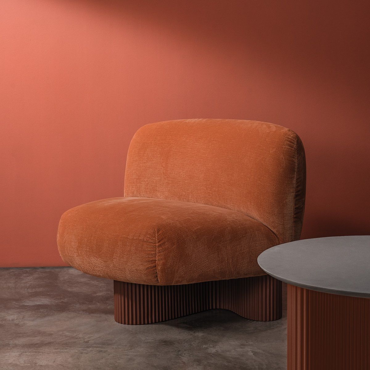 Bolete Lounge Sessel in Orange mit geriffeltem Sockel und passendem Beistelltisch vor farbiger Wand.