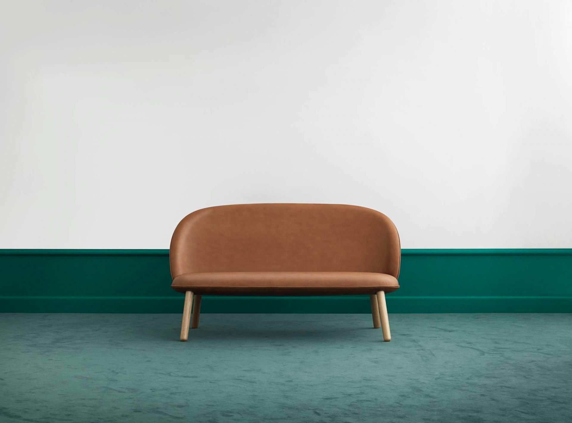 Ace Sofa von Normann Copenhagen in Brandy-Leder mit Holzbeinen vor grüner Wand.