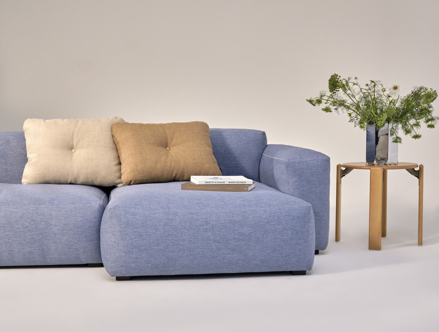 Blauer Loungesessel mit Kissen und Holzhocker mit Blumen, modernes Wohnzimmer-Interieur. Rey Stool Hocker Hay ähnlich.