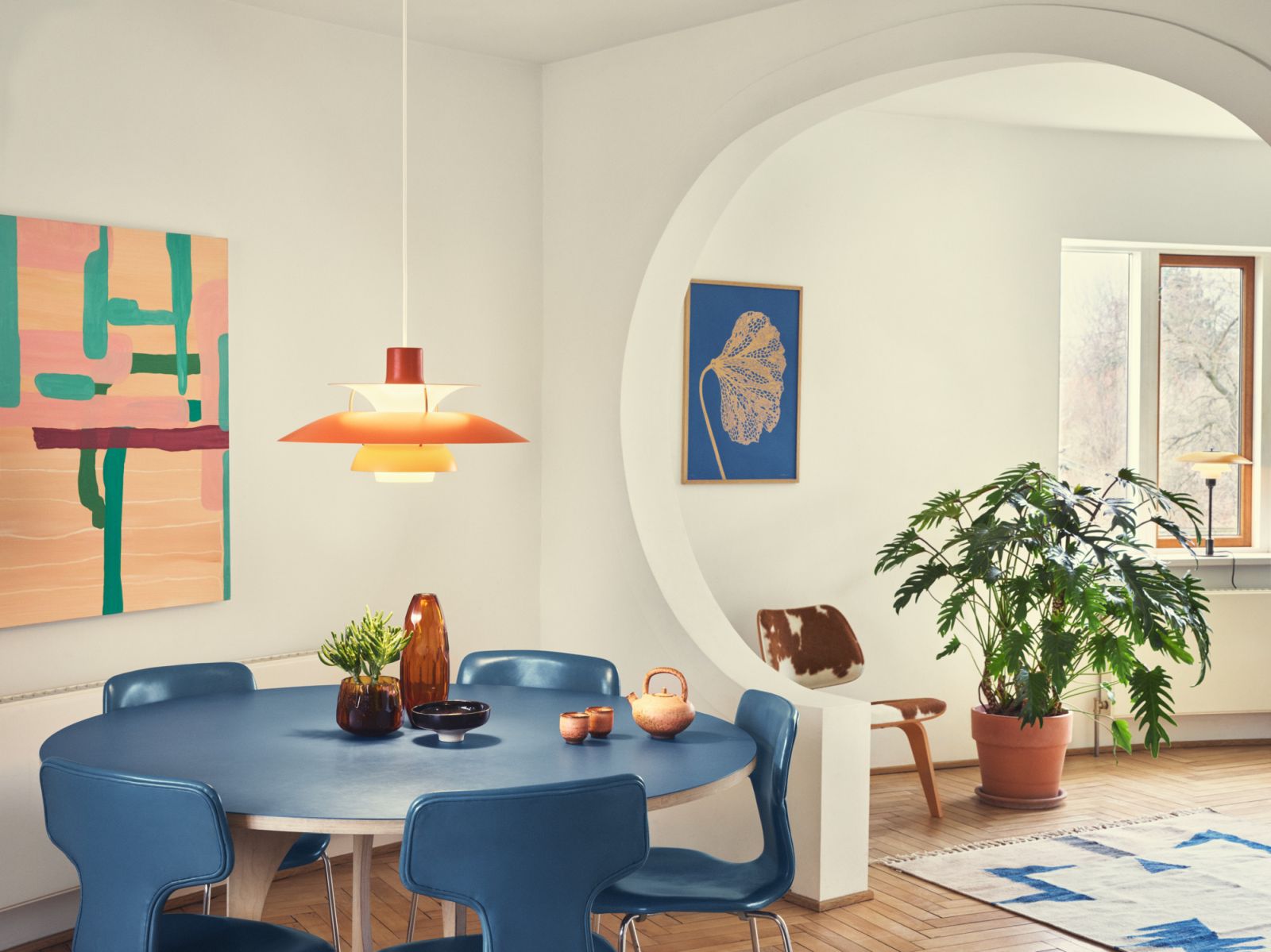 Orangefarbene PH 5 Pendelleuchte von Louis Poulsen über blauem Esstisch in modernem Wohnzimmer.