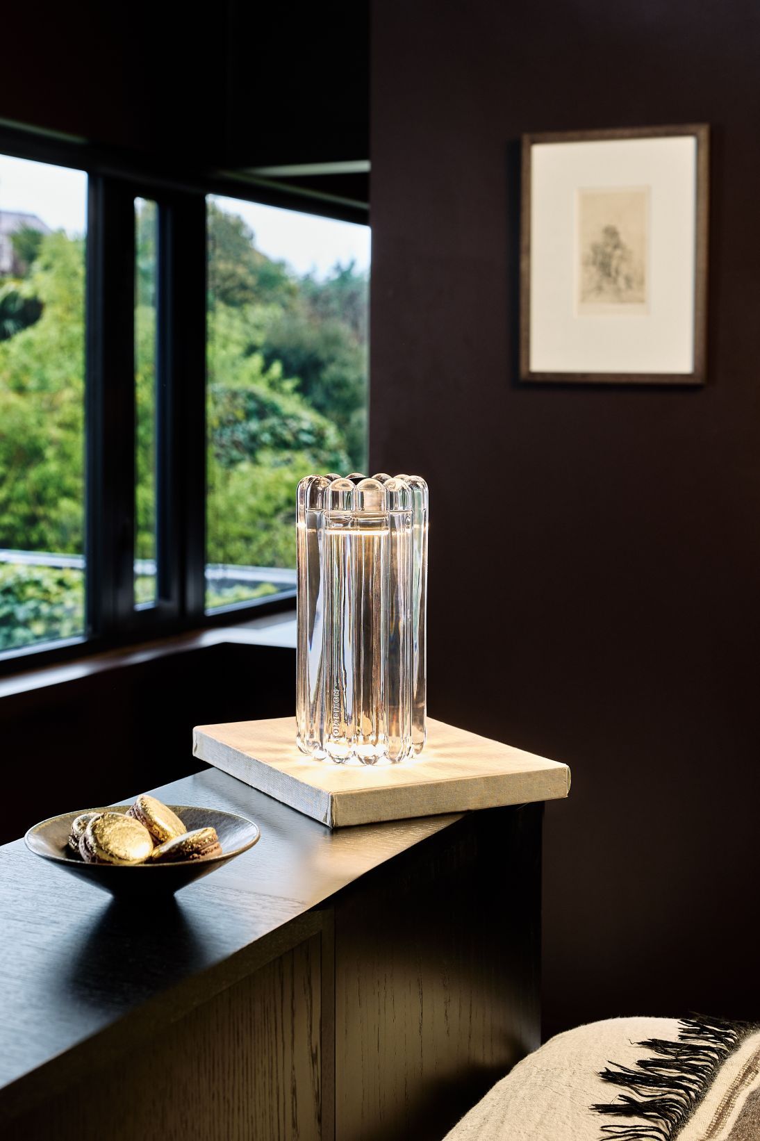 Tom Dixon Press Tischleuchte aus klarem Glas auf einem Nachttisch mit Dekoration im Schlafzimmer.