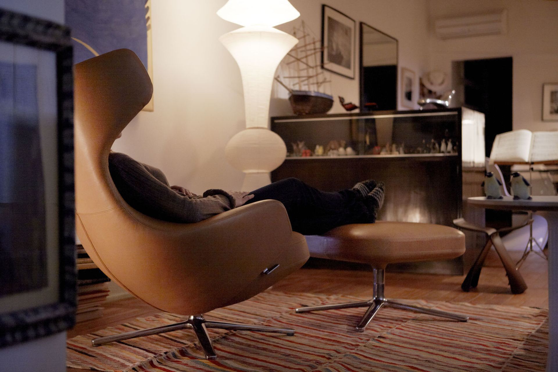 Person entspannt im Ledersessel mit passendem Hocker, im Hintergrund Vitra Butterfly Stool Hocker sichtbar.
