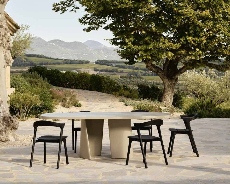Ethnicraft Canyon Outdoor Esstisch aus Beton mit schwarzen Stühlen im Garten mit Landschaft im Hintergrund.