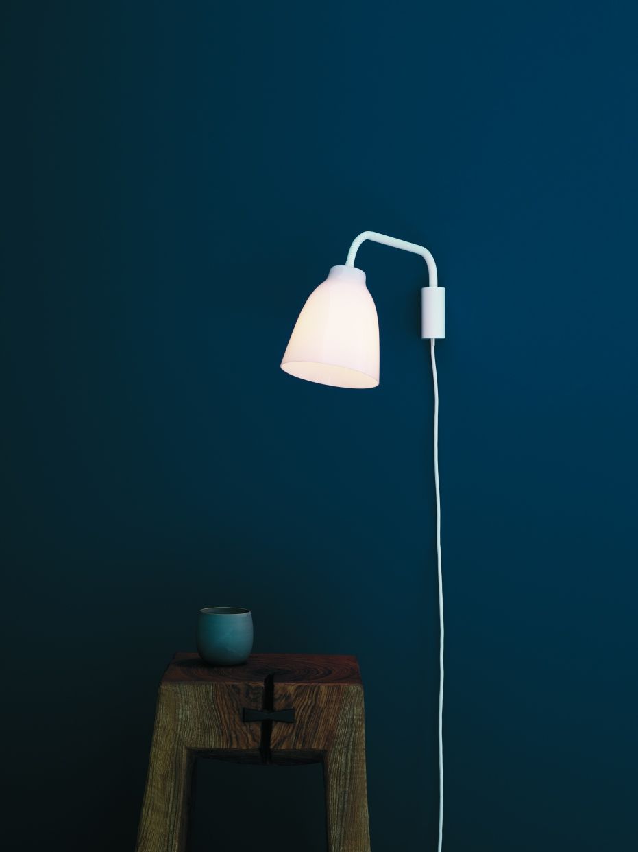Weiße Caravaggio Read Wandleuchte von Fritz Hansen an blauer Wand, mit Holzhocker und Deko.