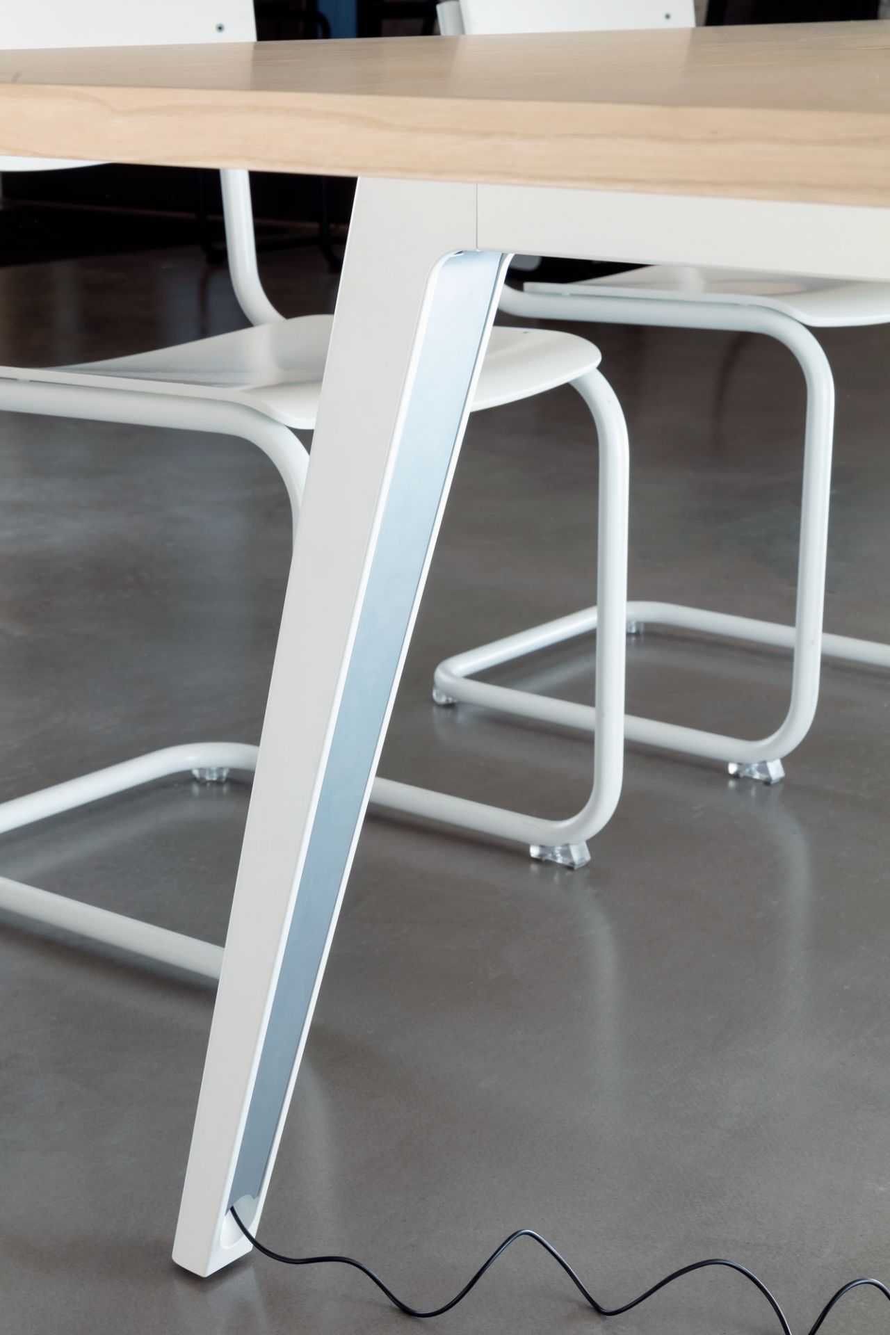 Detailaufnahme vom Bein des Thonet 1500 Tisches mit weißem Gestell und hellem Holztischblatt, Kabel am Boden.