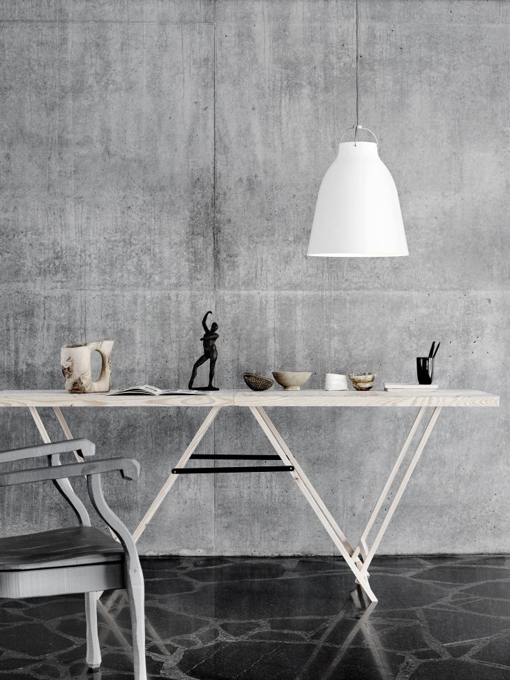 Weiße Caravaggio Pendelleuchte von Fritz Hansen über einem Holztisch mit Dekorationsgegenständen vor einer Betonwand.