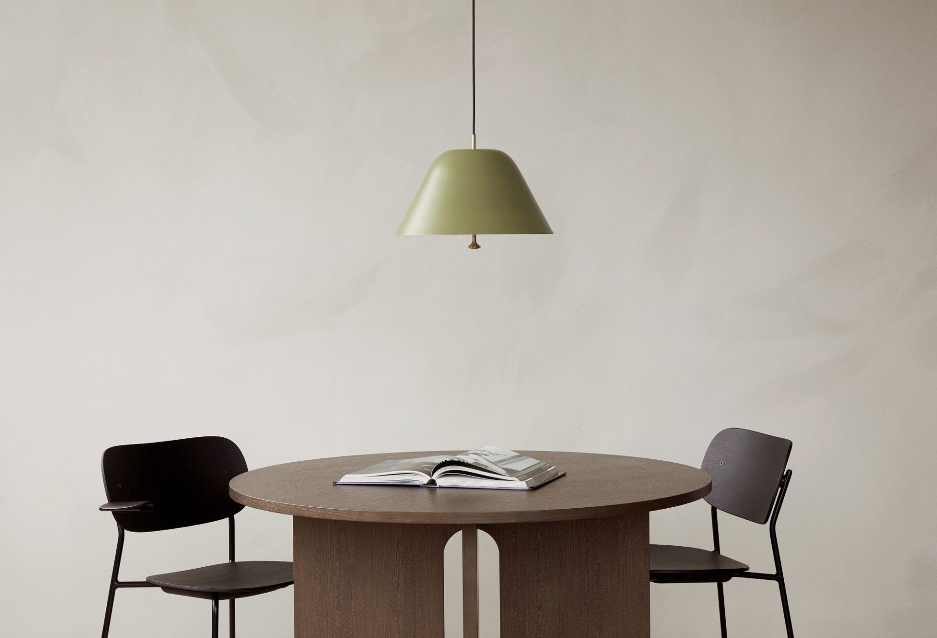 Audo Copenhagen Co Dining Chair Stuhl an rundem Esstisch mit Buch und grüner Lampe.