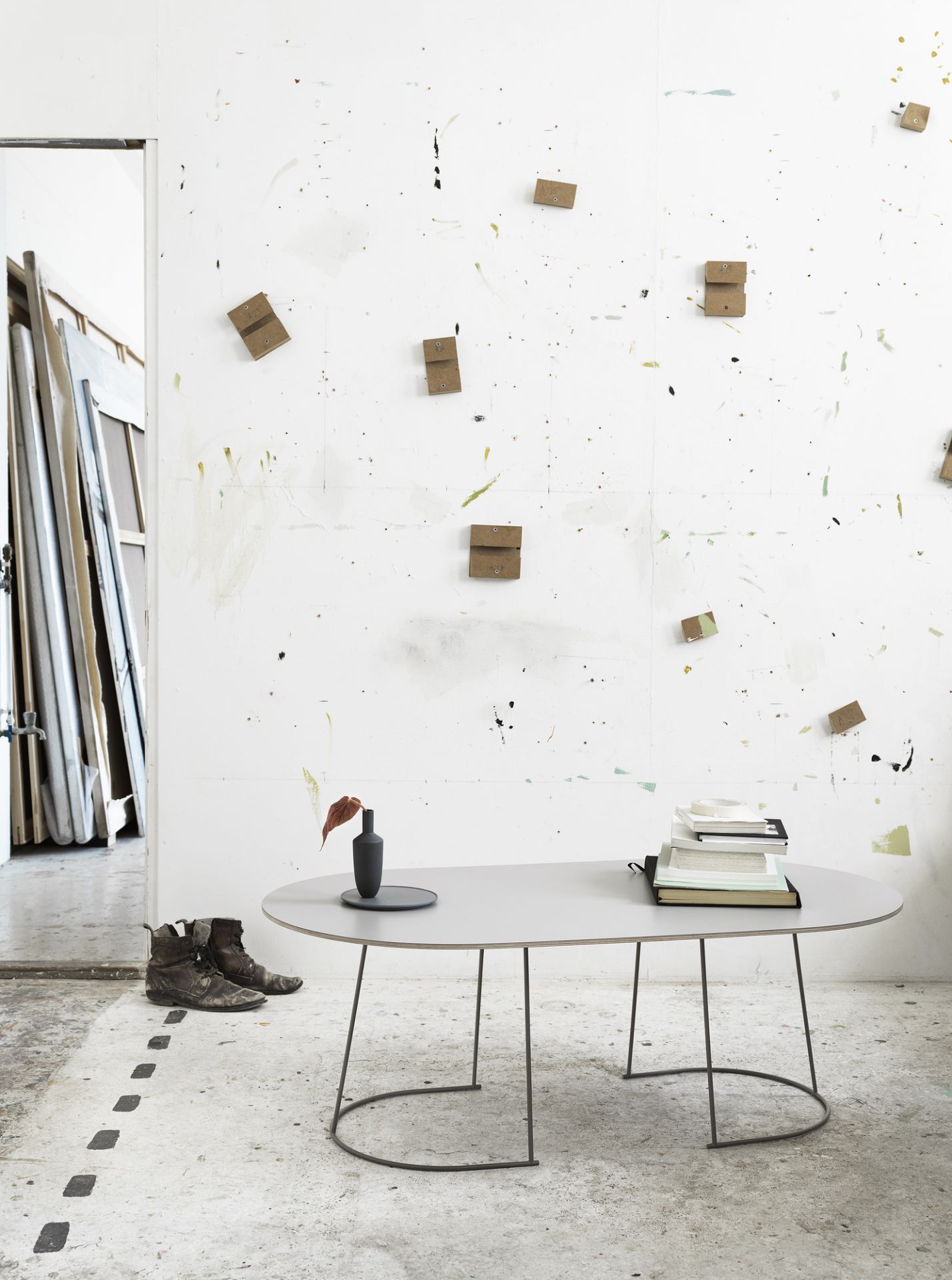 Muuto Airy Coffee Table Large: Ovaler Couchtisch in Grau mit filigranem Metallgestell in einem Atelier.