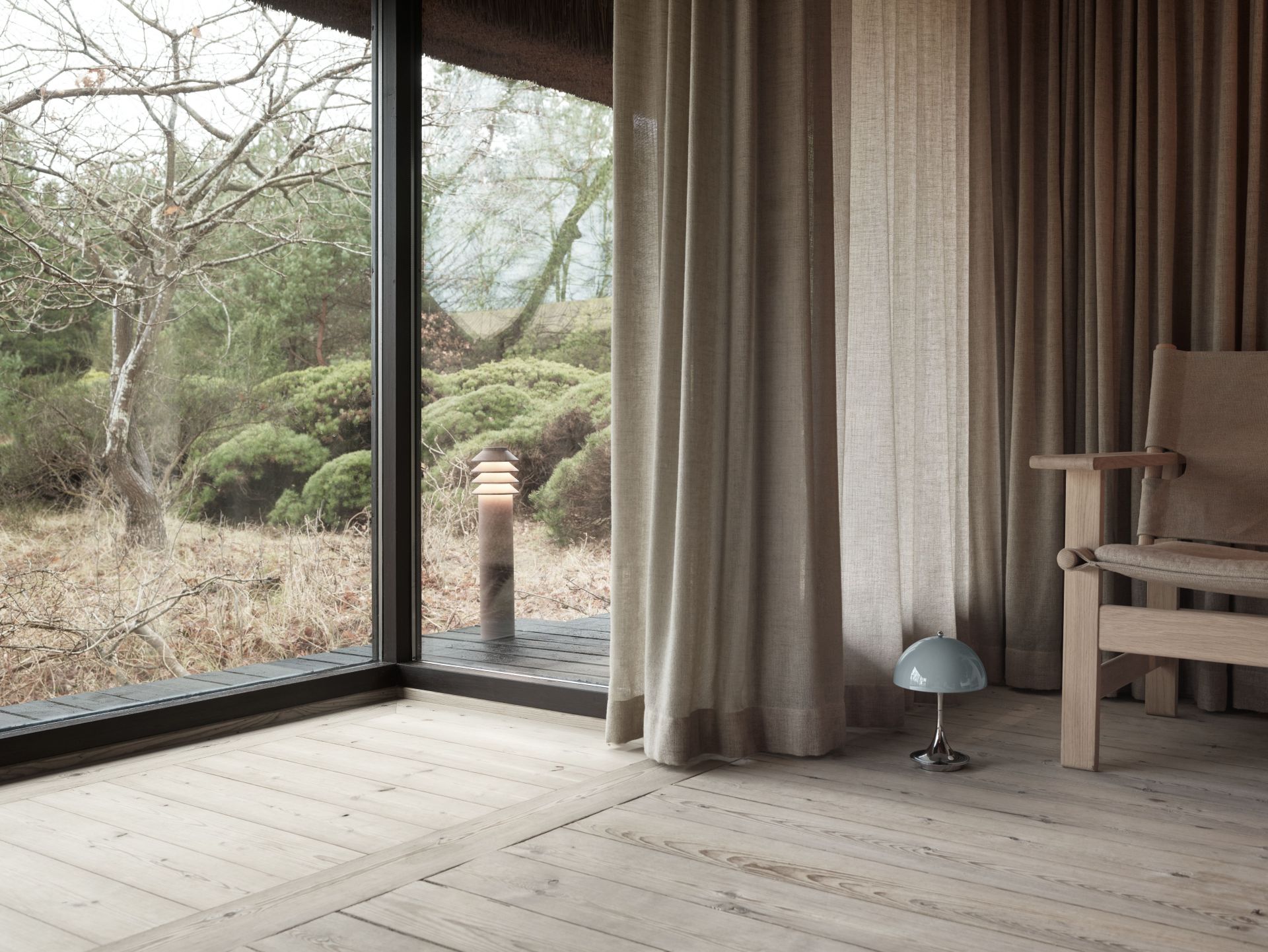 Innenaufnahme mit Louis Poulsen Bysted Garden Pollerleuchte, die durch ein Fenster eine stimmungsvolle Außenbeleuchtung erzeugt.