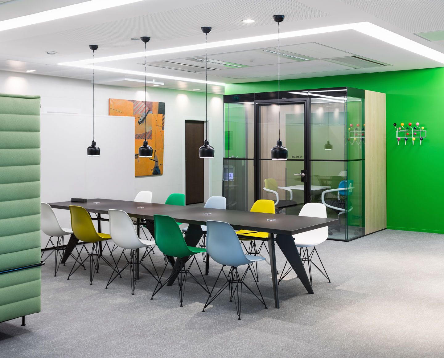 Büro mit Esstisch und mehreren bunten Eames Fiberglass Chair DSR Stühlen von Vitra mit Sitzpolster.