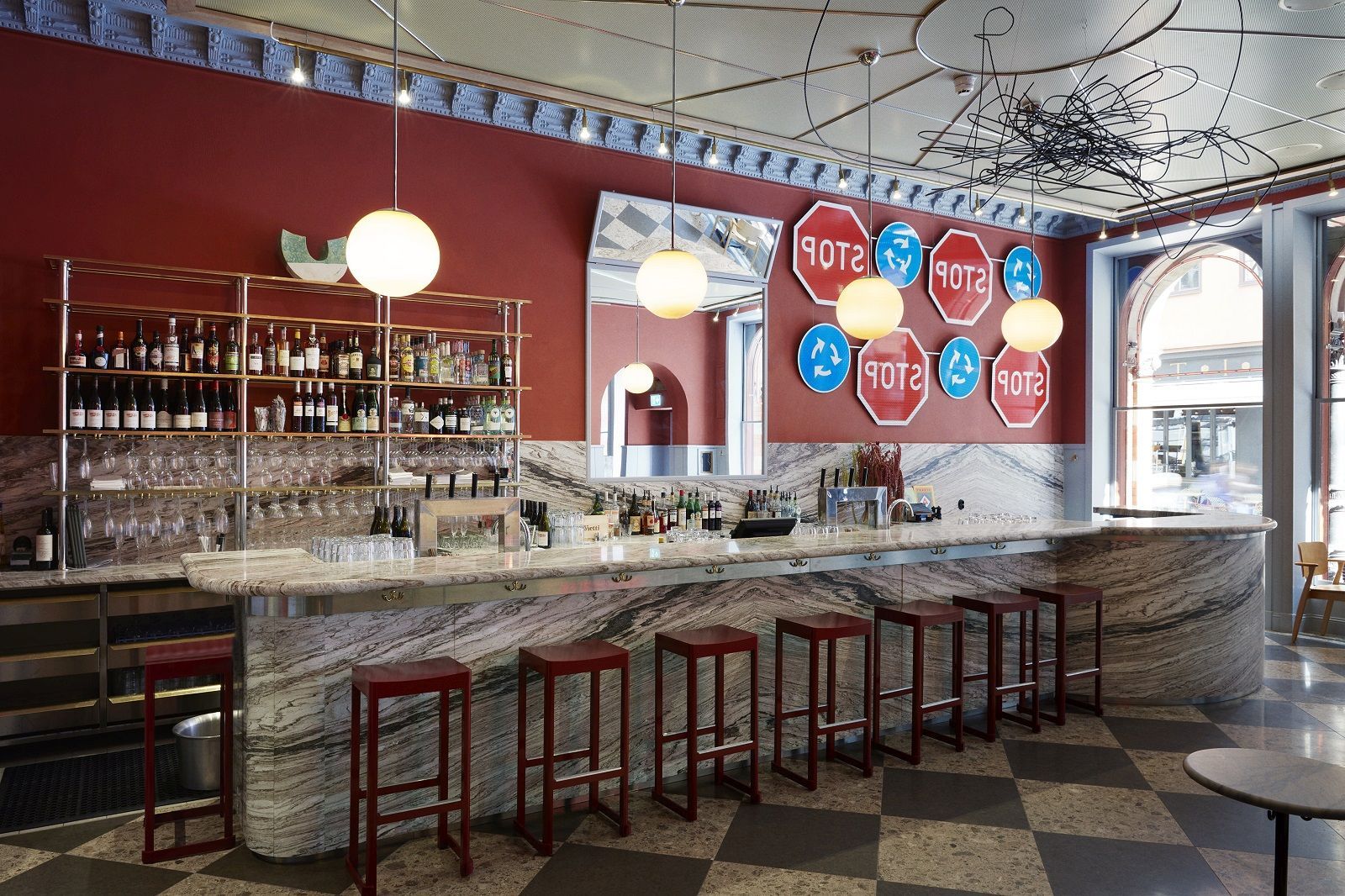 Rote Atelier Bar Stool Barhocker von Artek an einer Bar mit Marmorplatte und Spirituosenregal.