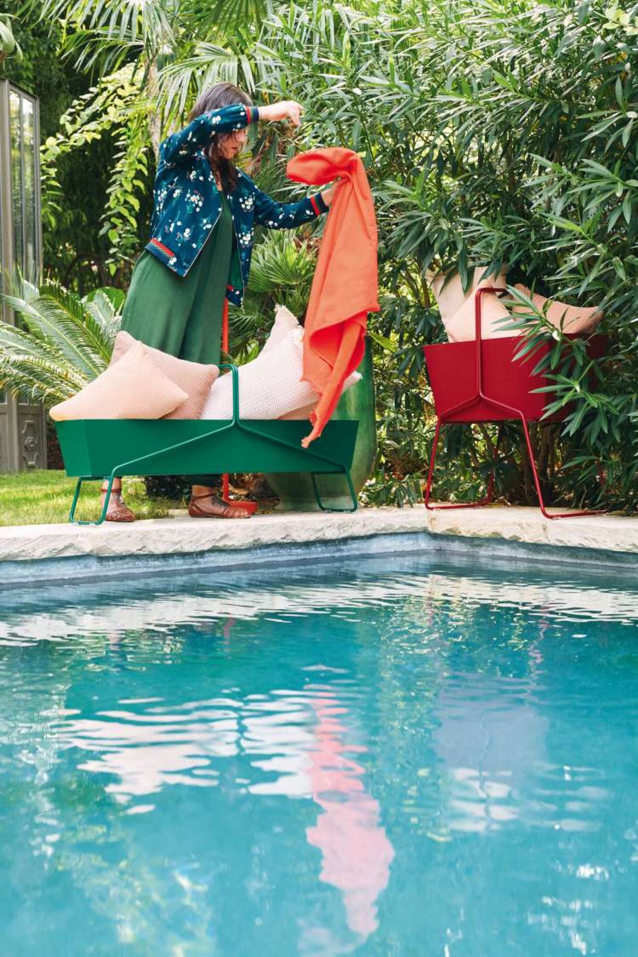 Frau drapiert Tuch über grünen Fermob Basket Blumenkasten hoch am Pool, roter Blumenkasten im Hintergrund.