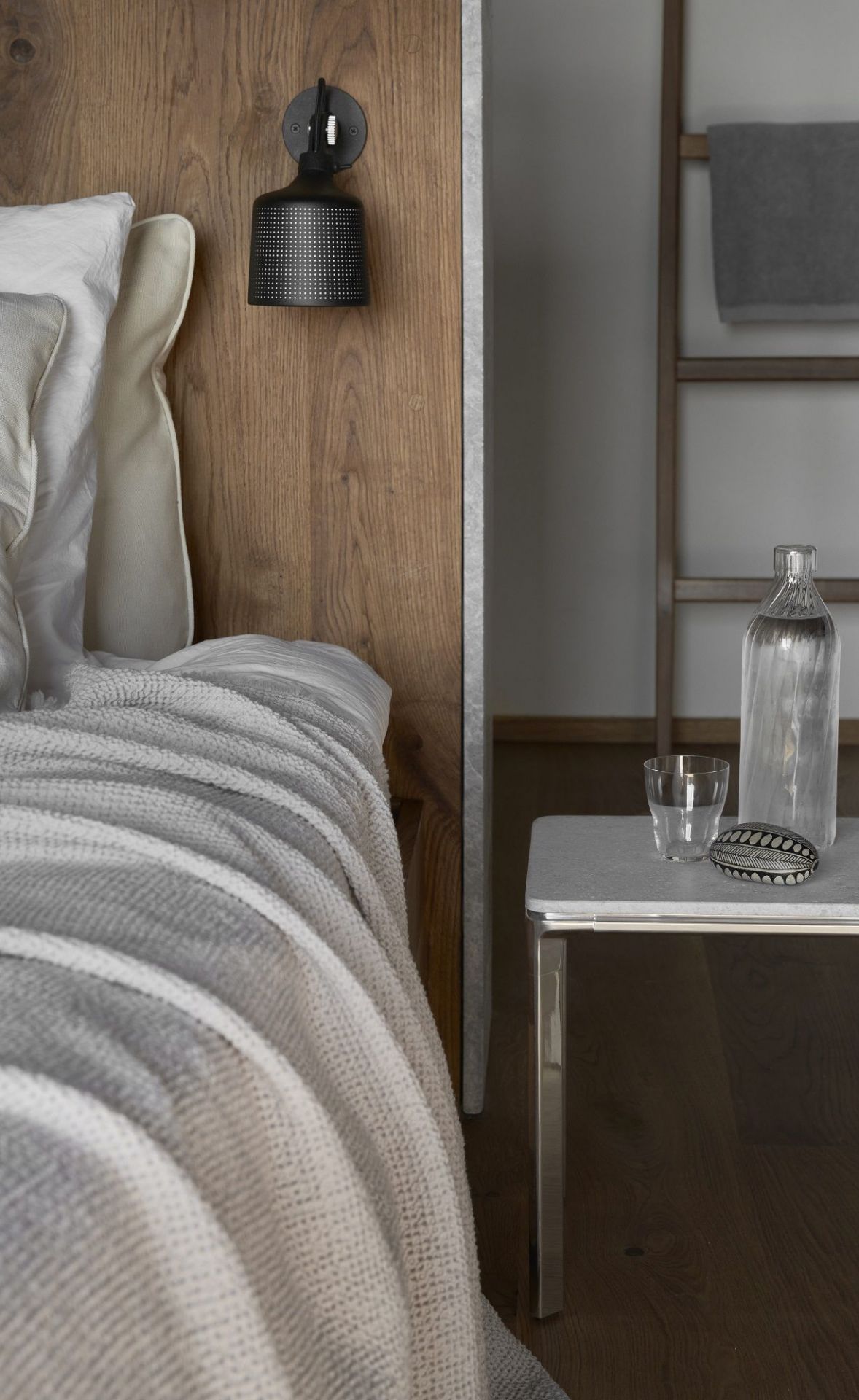 Nahaufnahme eines Vipp Nachttisches mit Wasserflasche und Glas neben einem Bett.