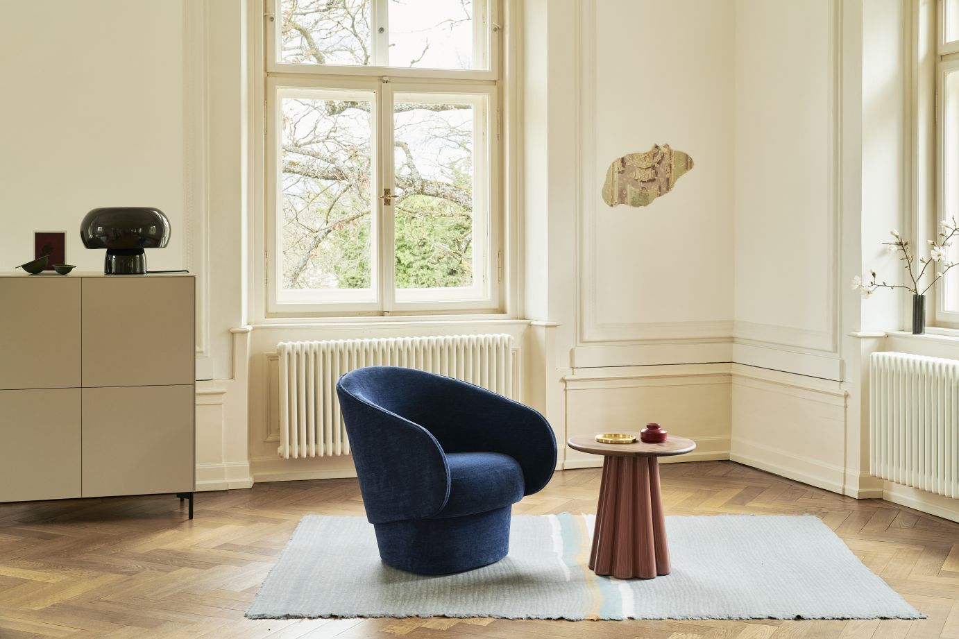 Bromo Beistelltisch Favius aus Holz im Wohnzimmer, neben einem blauen Sessel auf einem Teppich.