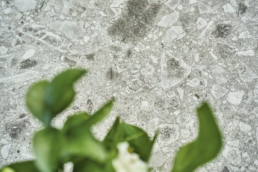 Detailaufnahme der Tischplatte vom Weishäupl Slope Outdoor Tisch mit Terrazzo-Muster und grünen Blättern.