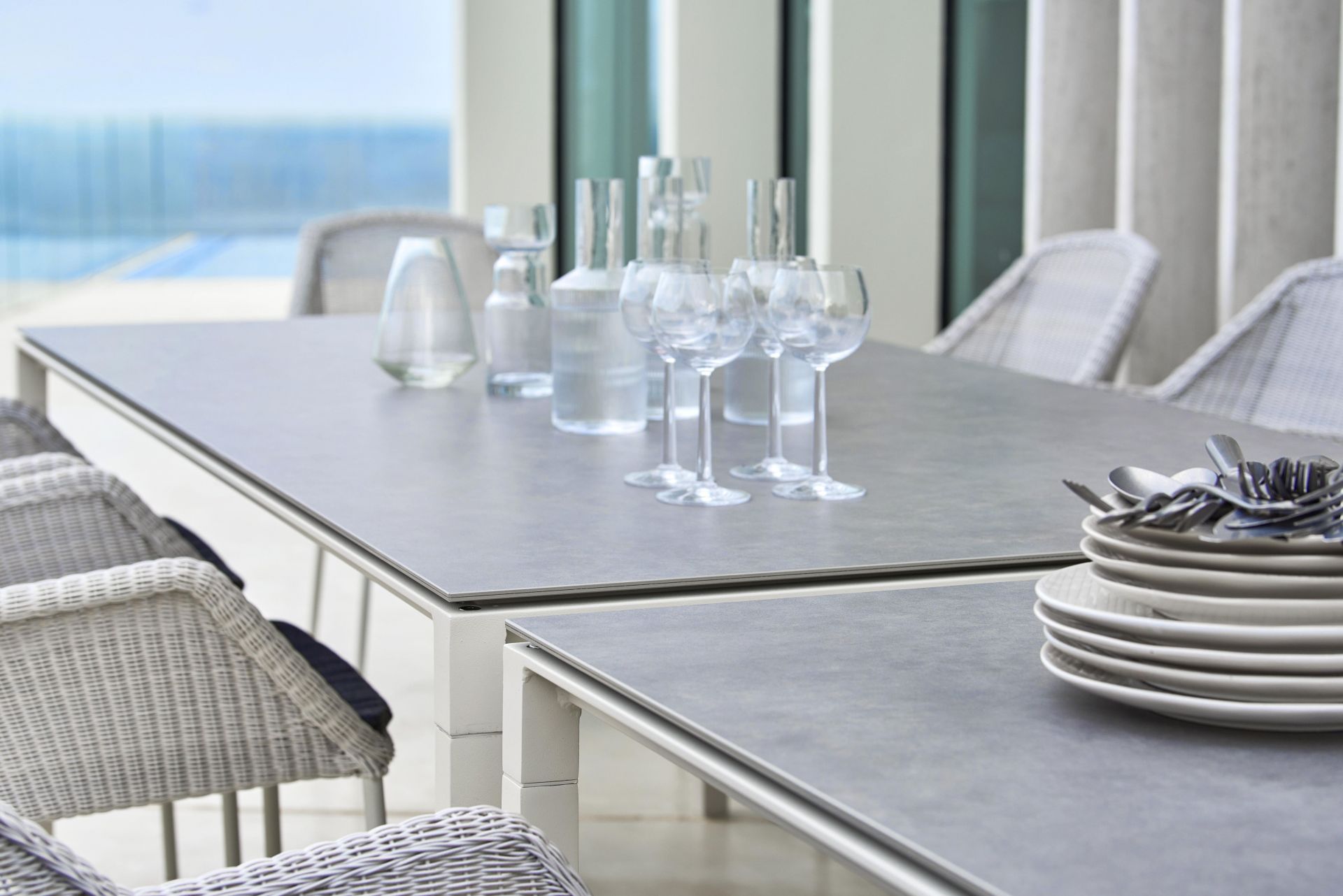 Cane-Line Pure Outdoor Esstisch mit Geschirr, Gläsern und Rattanstühlen auf einer Terrasse.