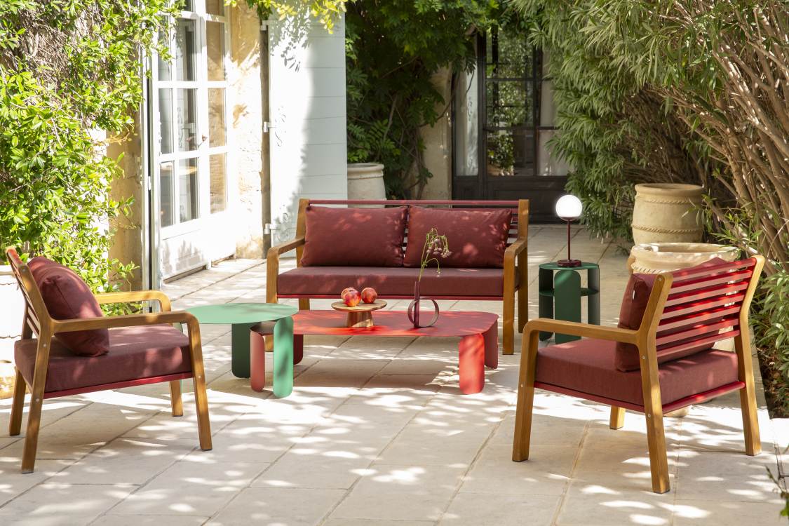 Somerset 2-Sitzer Outdoor Sofa von Fermob mit Sesseln und Tisch in einem Garten.