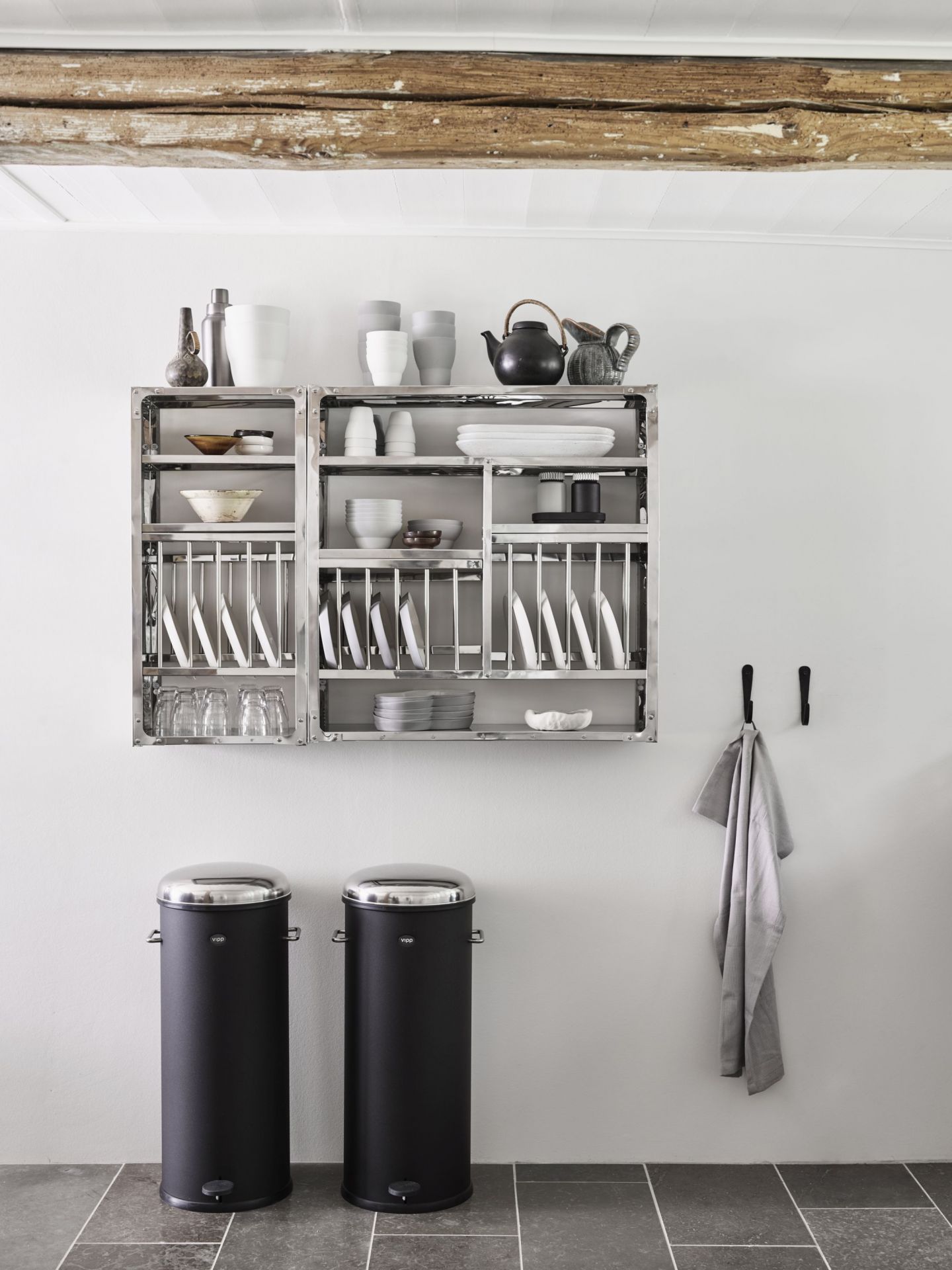 Zwei schwarze Vipp Treteimer mit Edelstahldeckel stehen in einer modernen Küche vor einem Geschirrregal.