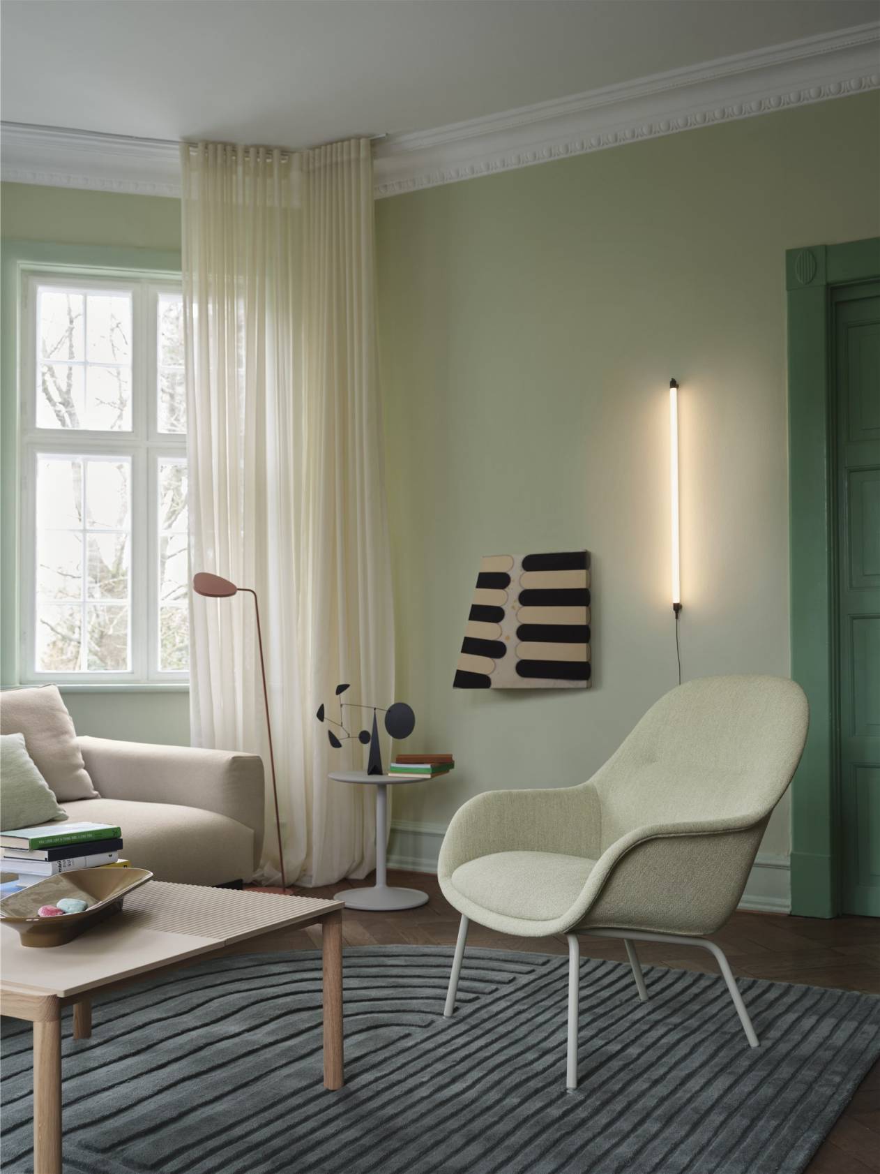 Helles Wohnzimmer mit Muuto Fine Wall Ceiling Wandleuchte, Sessel, Sofa und Teppich.