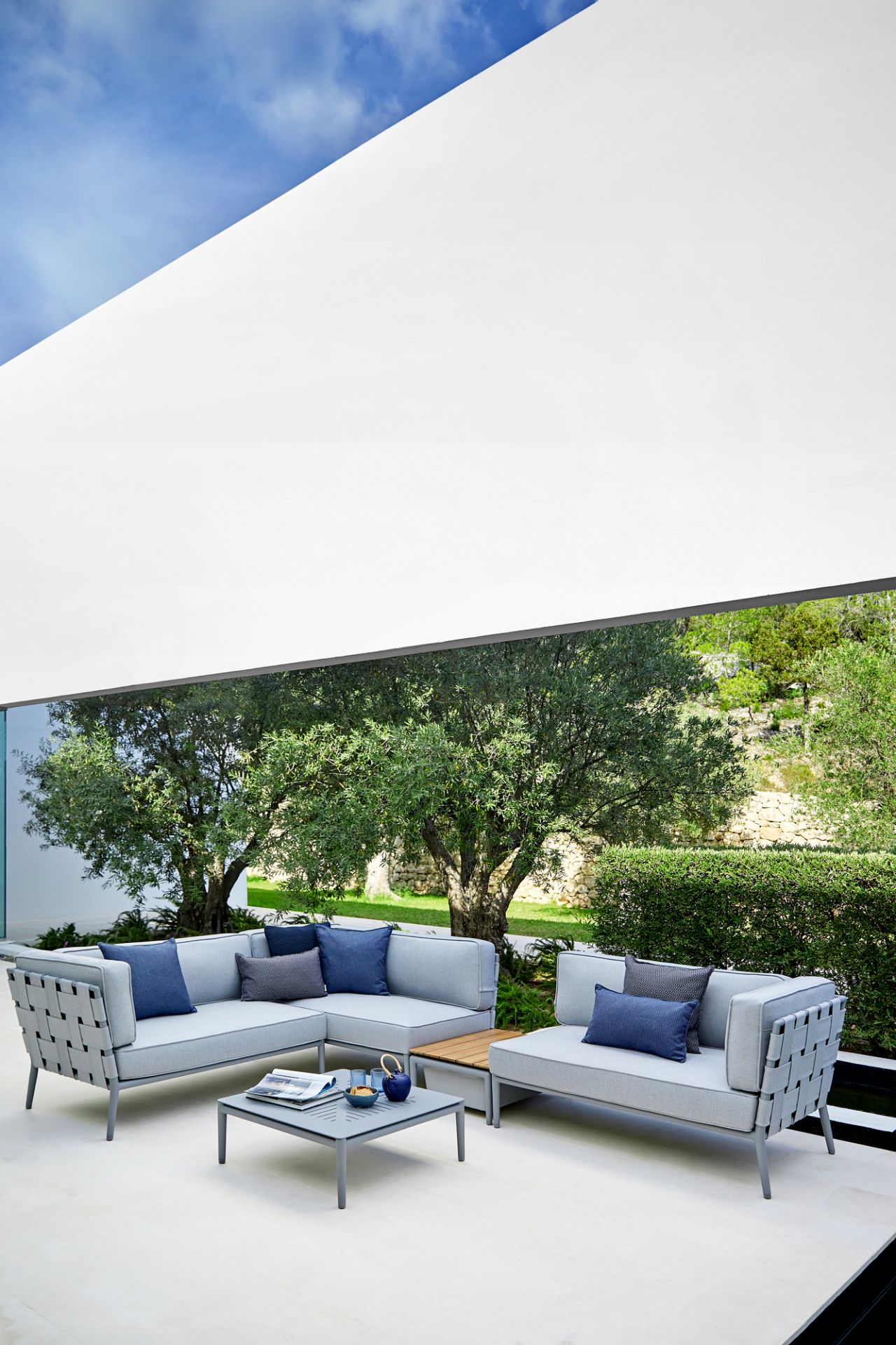 Helle Conic Outdoor Loungegruppe von Cane-Line mit Couchtisch und blauen Kissen im Garten.