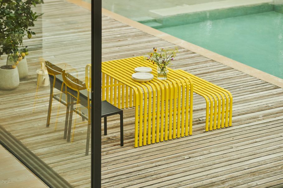 Gelbe Jan Kurtz Campus Bank Outdoor mit Stühlen auf einer Holzterrasse am Pool.