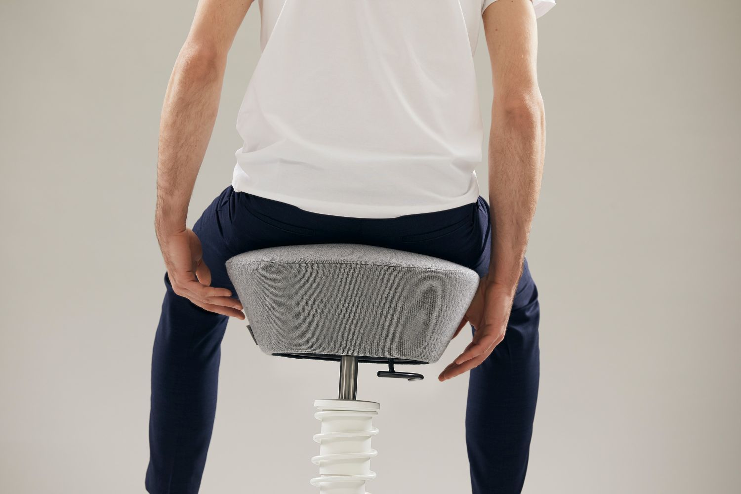 Mann sitzt auf einem grauen, ergonomischen Bürohocker mit spiralförmigem, weißen Fuß und verstellbarer Höhe.