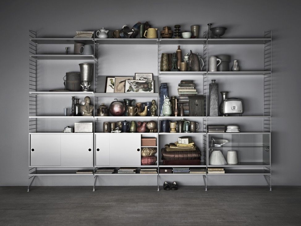 Graues String Furniture Regalsystem für das Wohnzimmer, vollgestellt mit Deko-Objekten und Büchern.