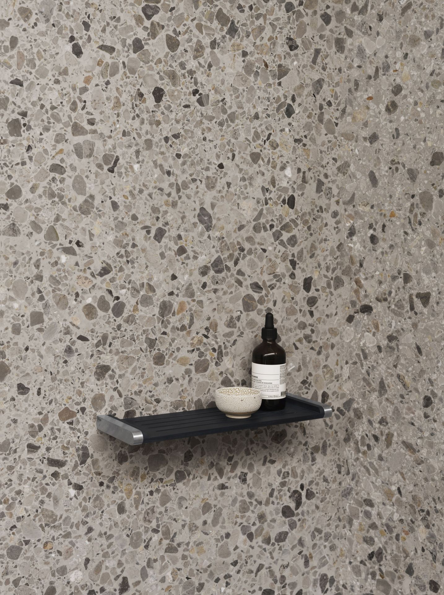 Schwarze Vipp Badablage mit Kosmetikprodukten an einer Terrazzo-Wand, moderne Badezimmer Ablage für Shampoo und Seife.