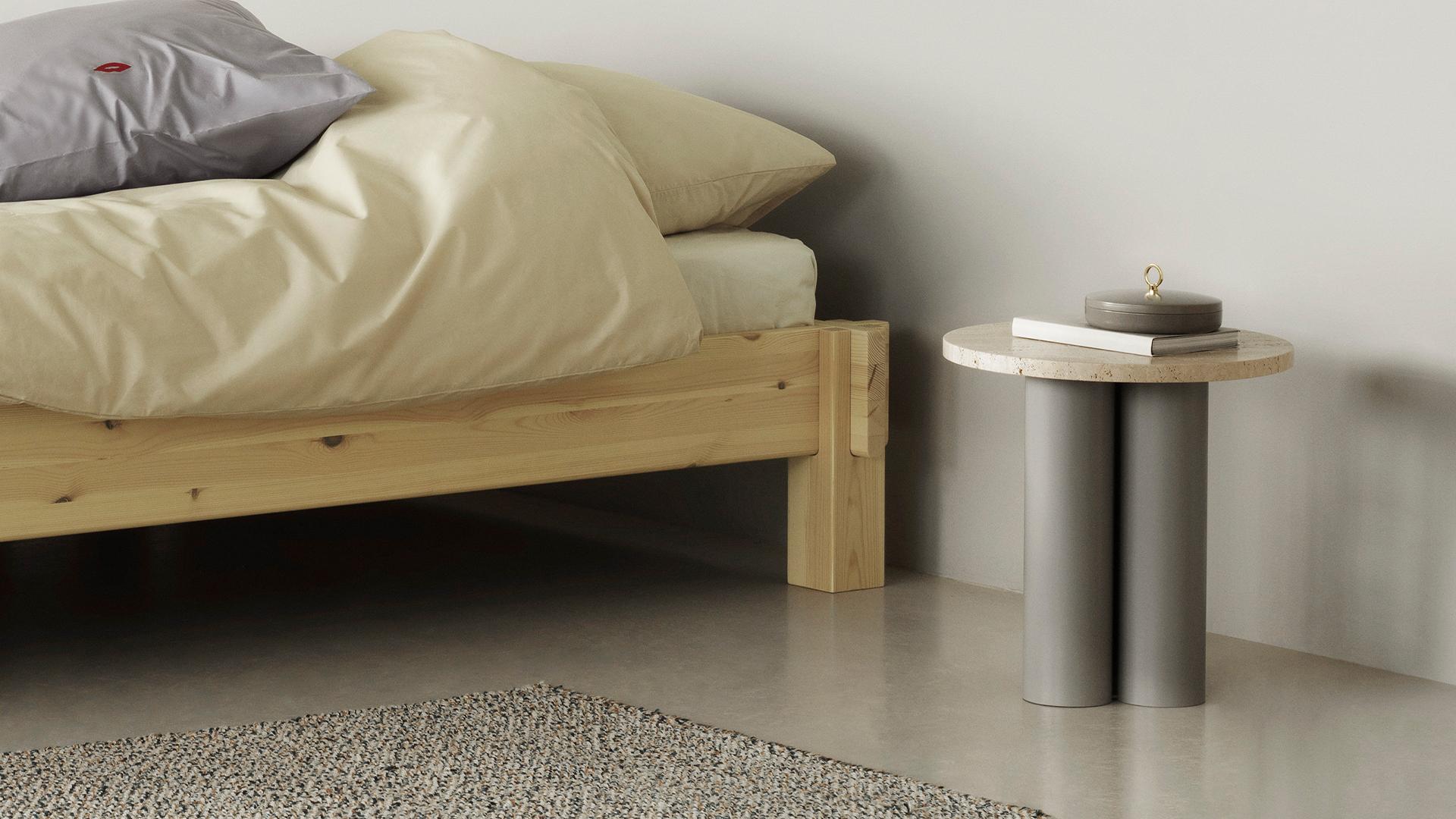 Normann Copenhagen Dit Coffee Table Beistelltisch aus Travertin und grauem Stahl neben einem Bett.