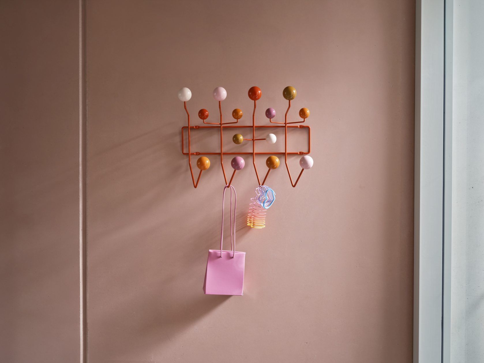 Eames Hang it all Garderobe Warm von Vitra an rosa Wand mit Tasche.