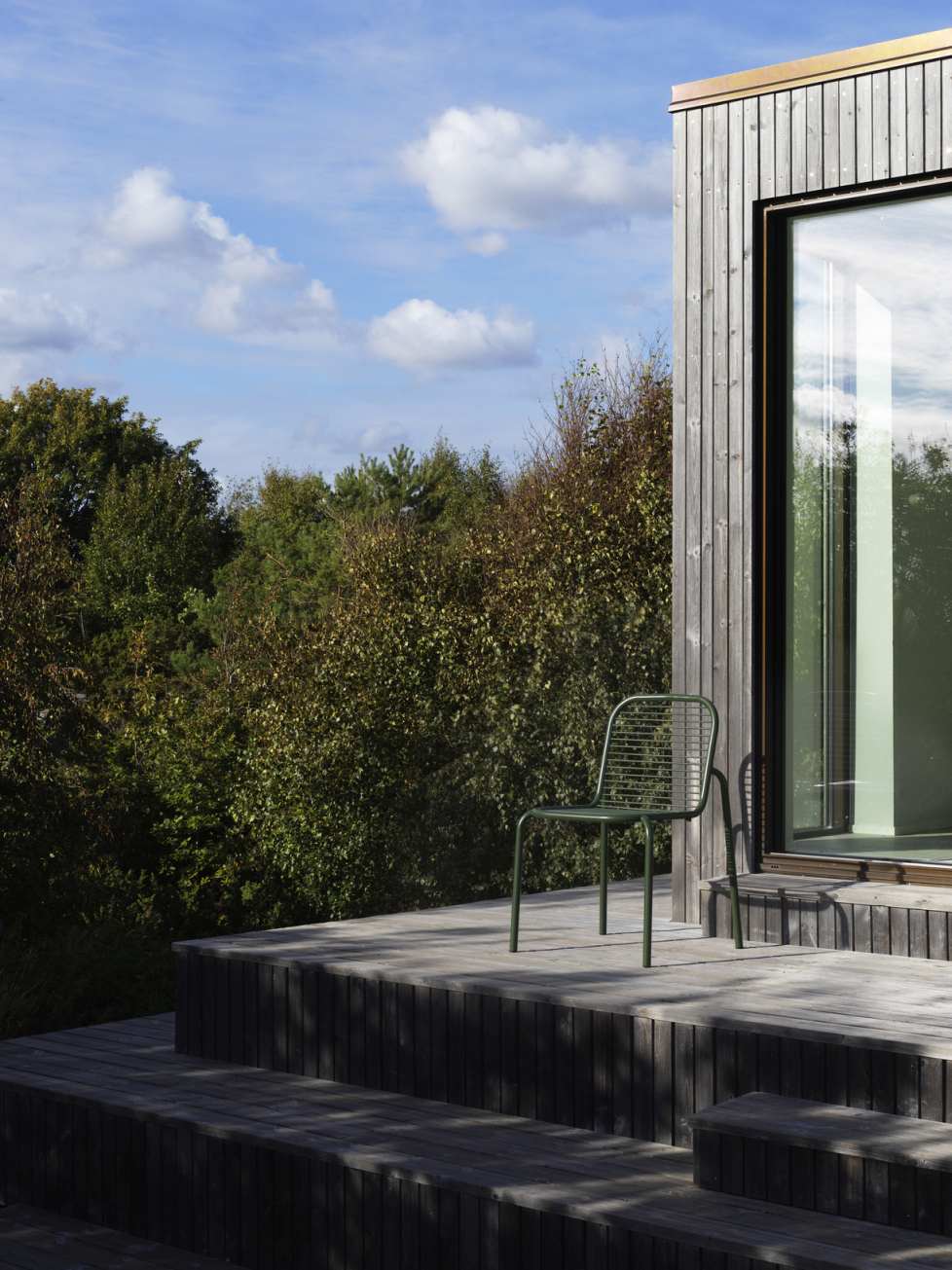 Grüner Vig Chair Stuhl von Normann Copenhagen auf Holzterrasse vor modernem Haus.