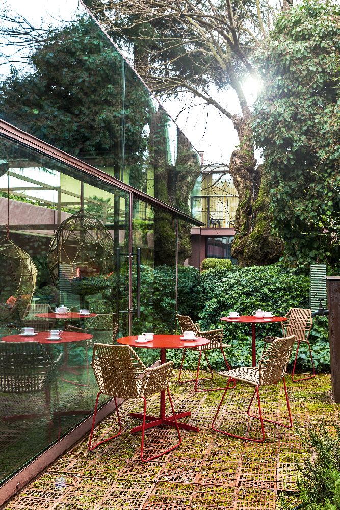 Tropicalia Armchair Outdoor von Moroso auf einer Terrasse mit roten Tischen und üppigem Grün.