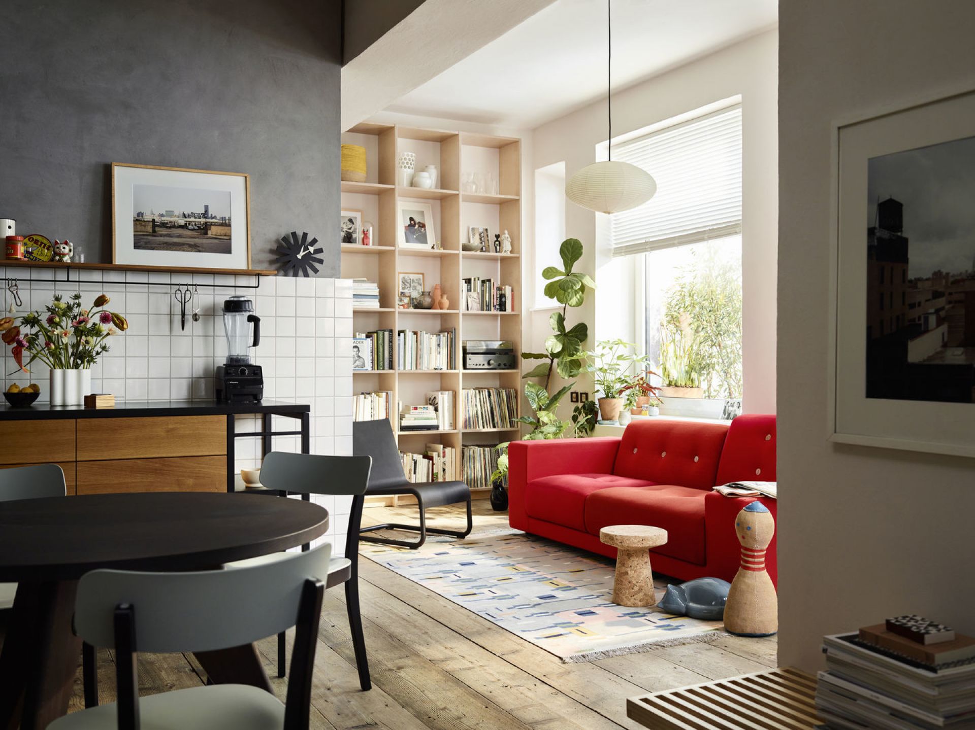 Wohnzimmer mit Vitra Akari Pendelleuchte, rotem Sofa, Holzboden und Bücherregal. Japanische Lampe für stimmungsvolle Beleuchtung.